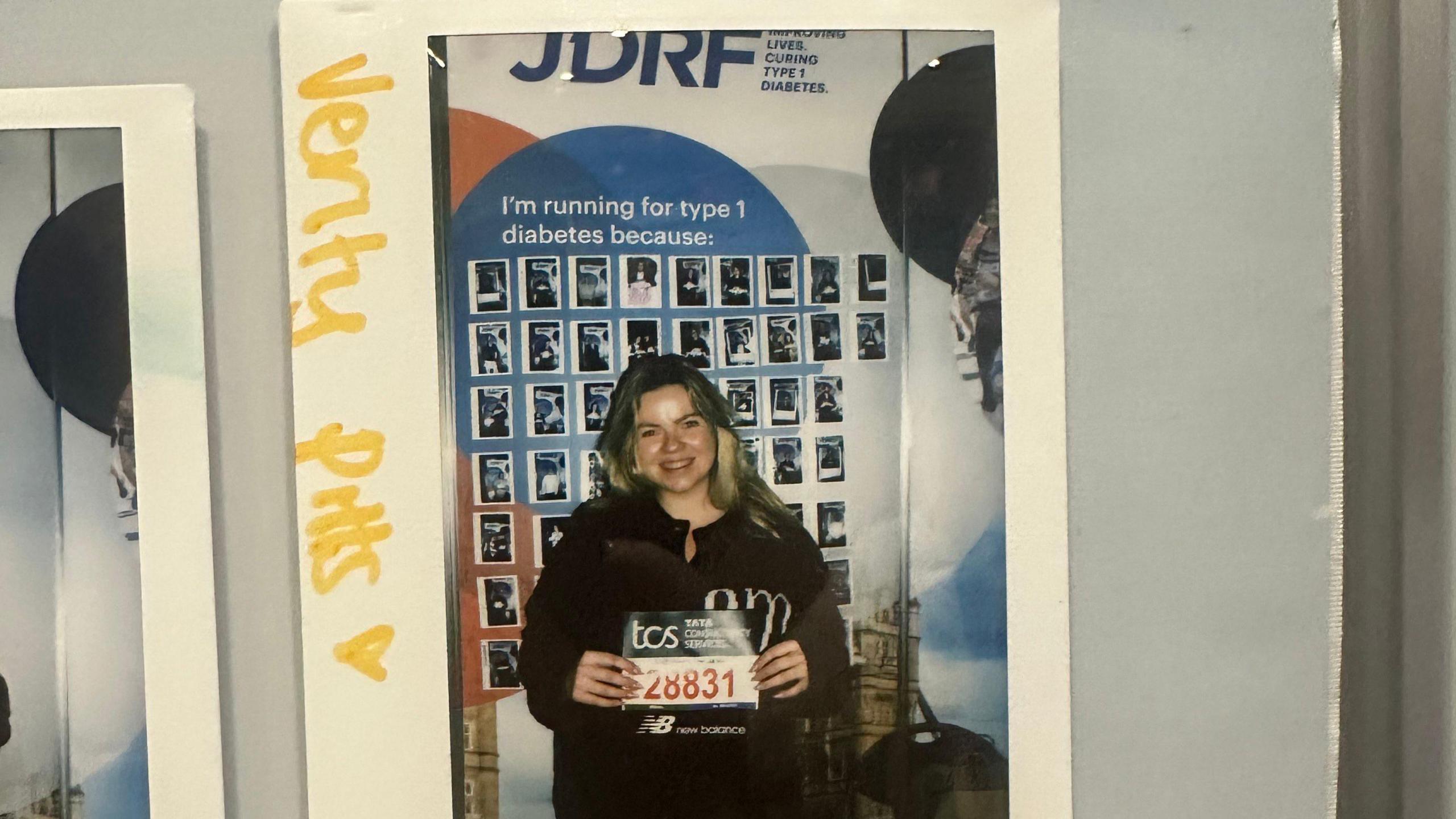 A polaroid image of Verity Pitts completing her first marathon. She is holding her race number '28831' while standing in front of a banner from Juvenile Diabetes Research Foundation, now known as Breakthrough T1D. It reads: 'I'm running for type 1 diabetes because...,' showing images of different people underneath.