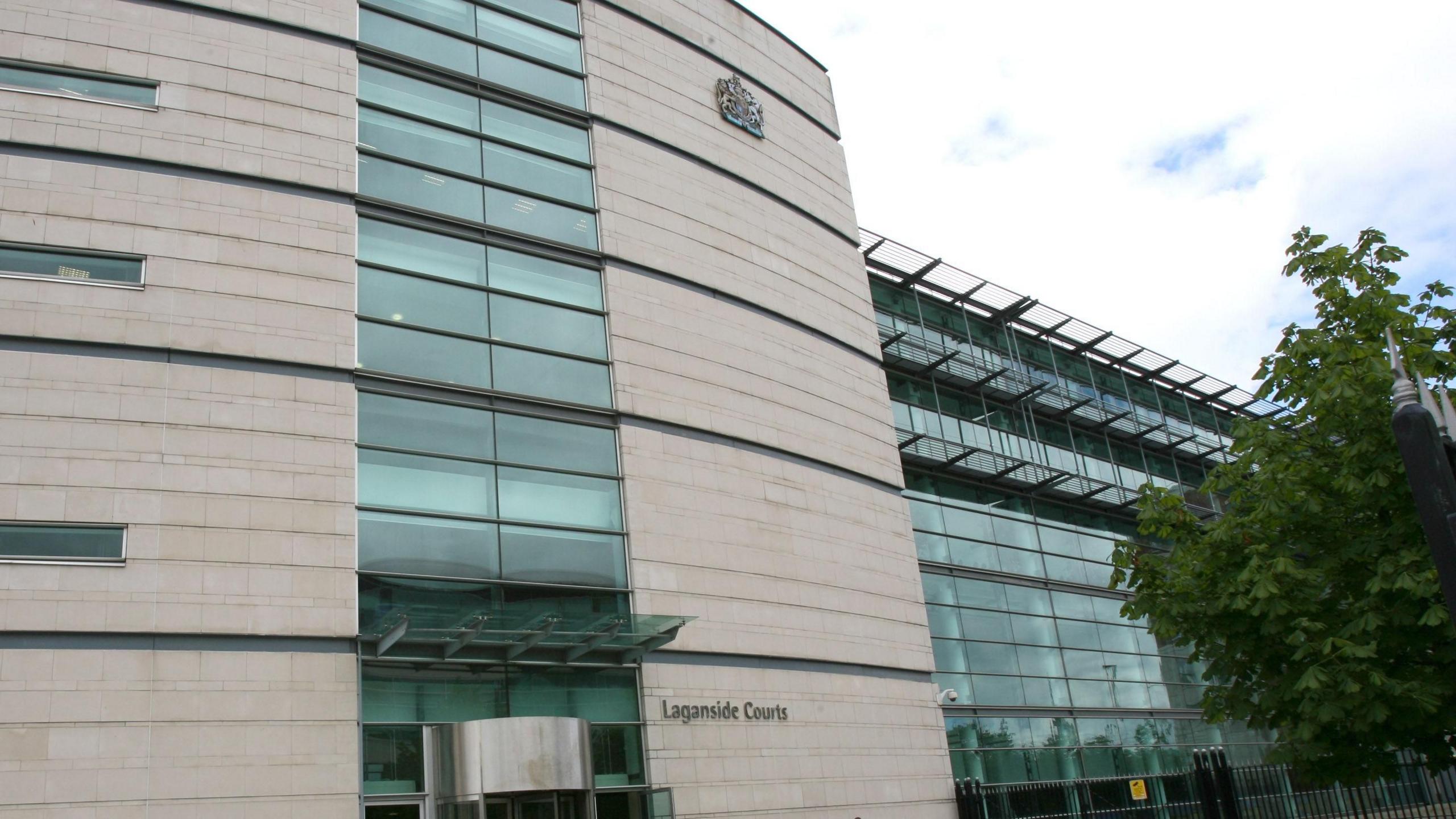 The front of the Laganside Courts in Belfast. The main building is brown with glass in the middle. The words Laganside Courts are on the bottom right. There is a glass building to the far right.