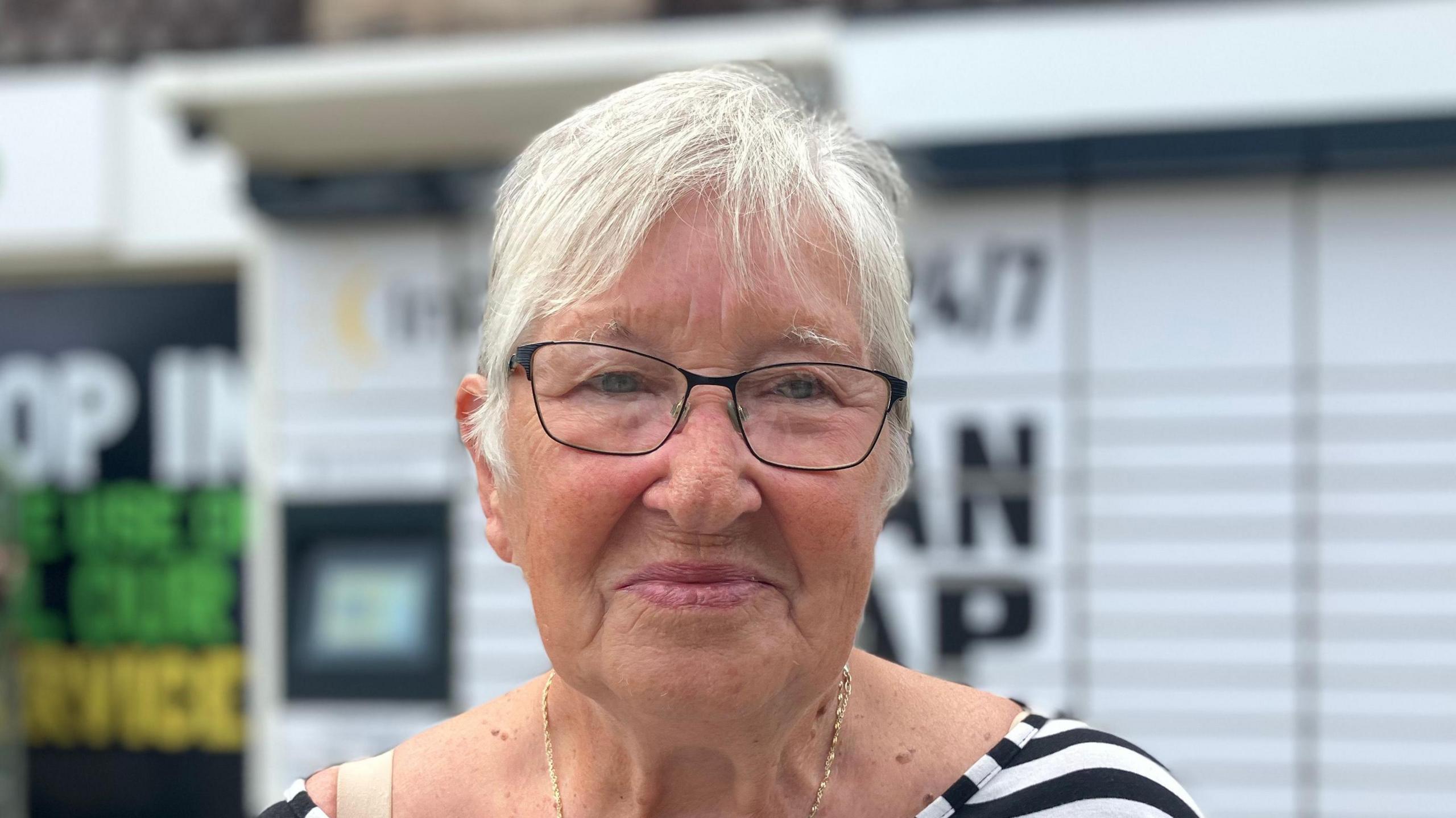 Marti Mower smiles at the camera. She has short grey hair and wears glasses and a black and white top. 
