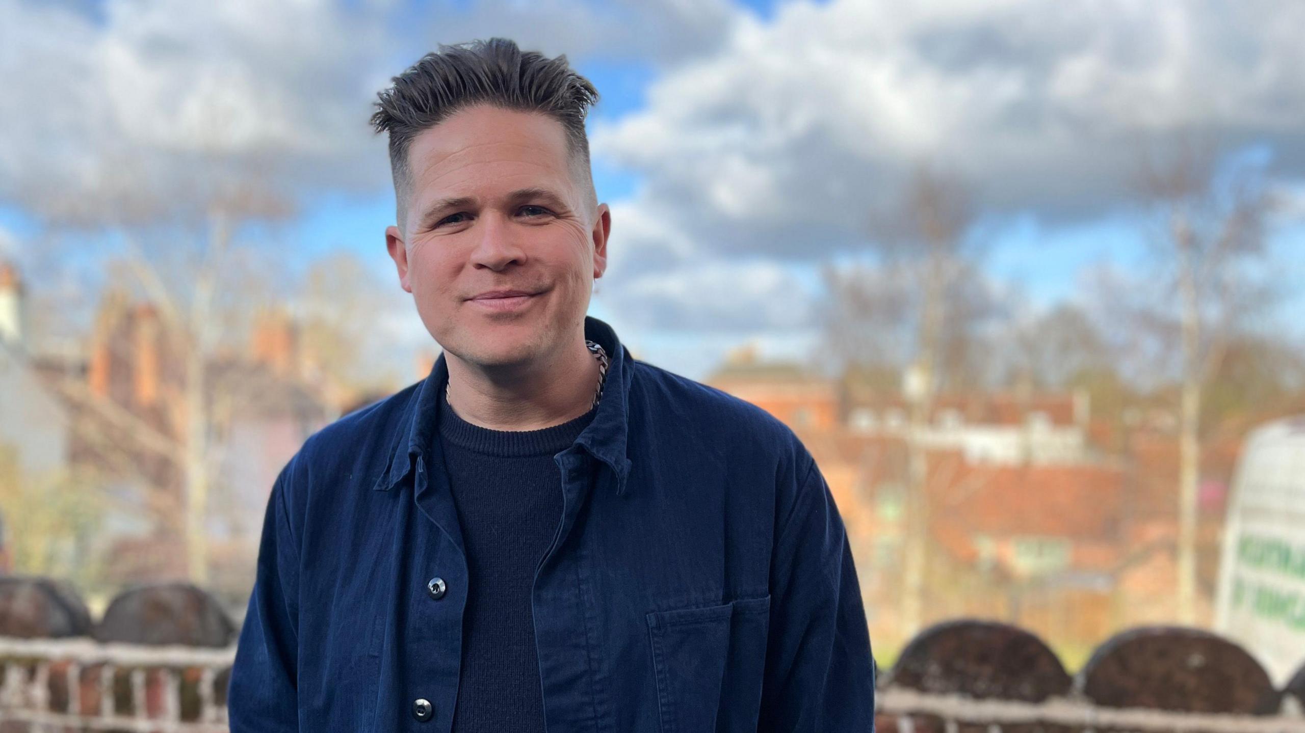 Luke Wright standing outside with a backdrop of trees and clouds.