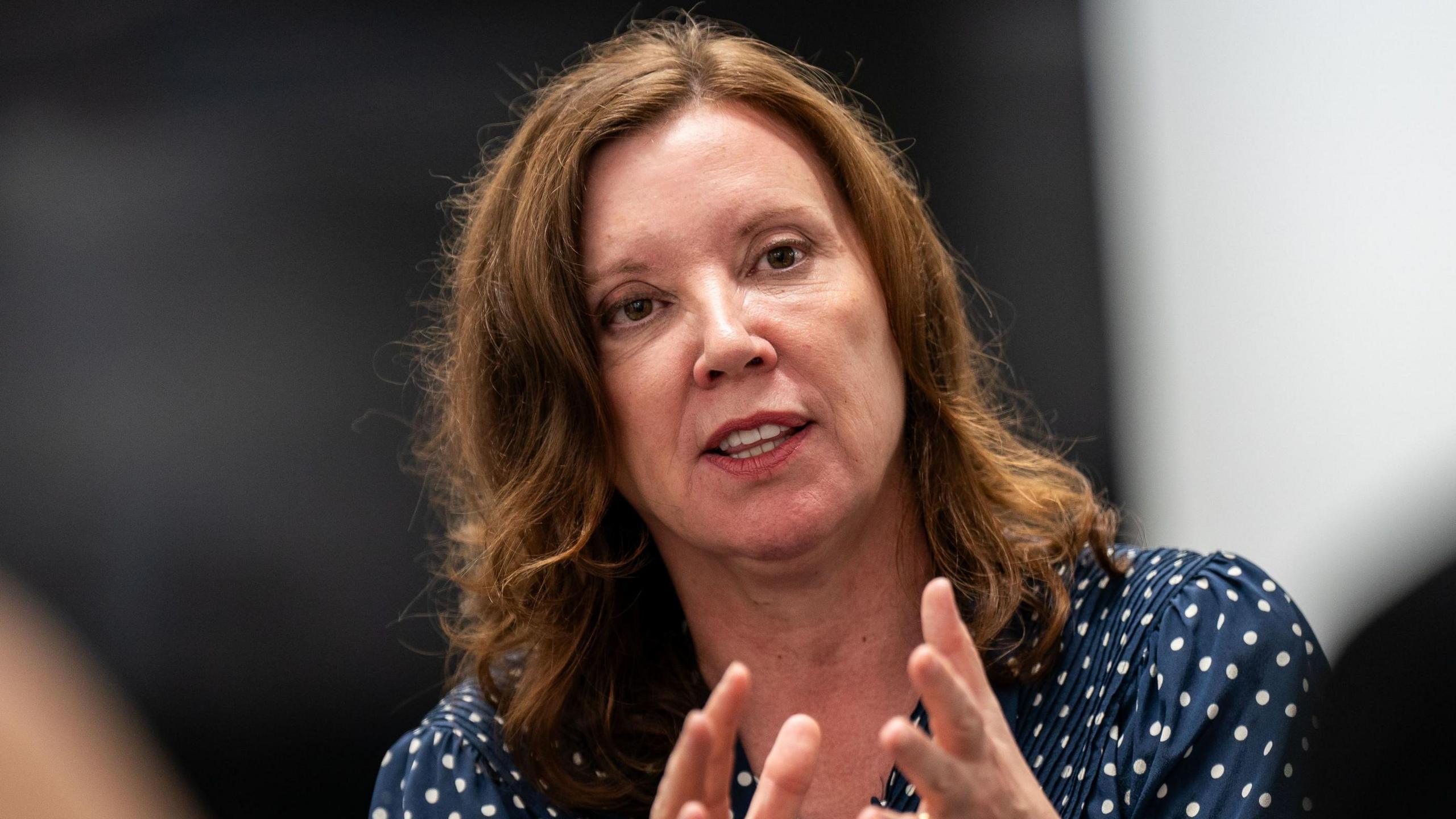 A head and shoulders image of Dame Rachel de Souza mid-speech. She has wavy brown hair worn loose to her shoulders and is wearing a navy blue coloured blouse with white polka dots.