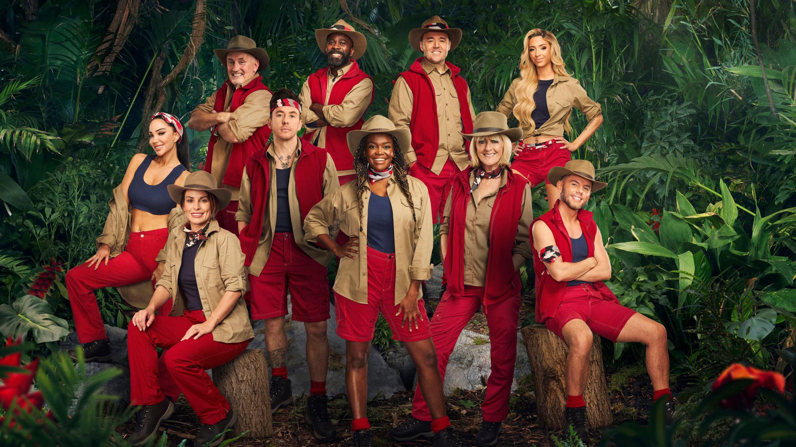 Press shot of Tulisa, Coleen, Barry, Danny, Melvin, Oti, Alan, Jane, GK Barry & Dean, who took part in series 24 of I’m a Celebrity Get Me Out of Here. The camp mates are dressed in red, blue and brown camp wear. 