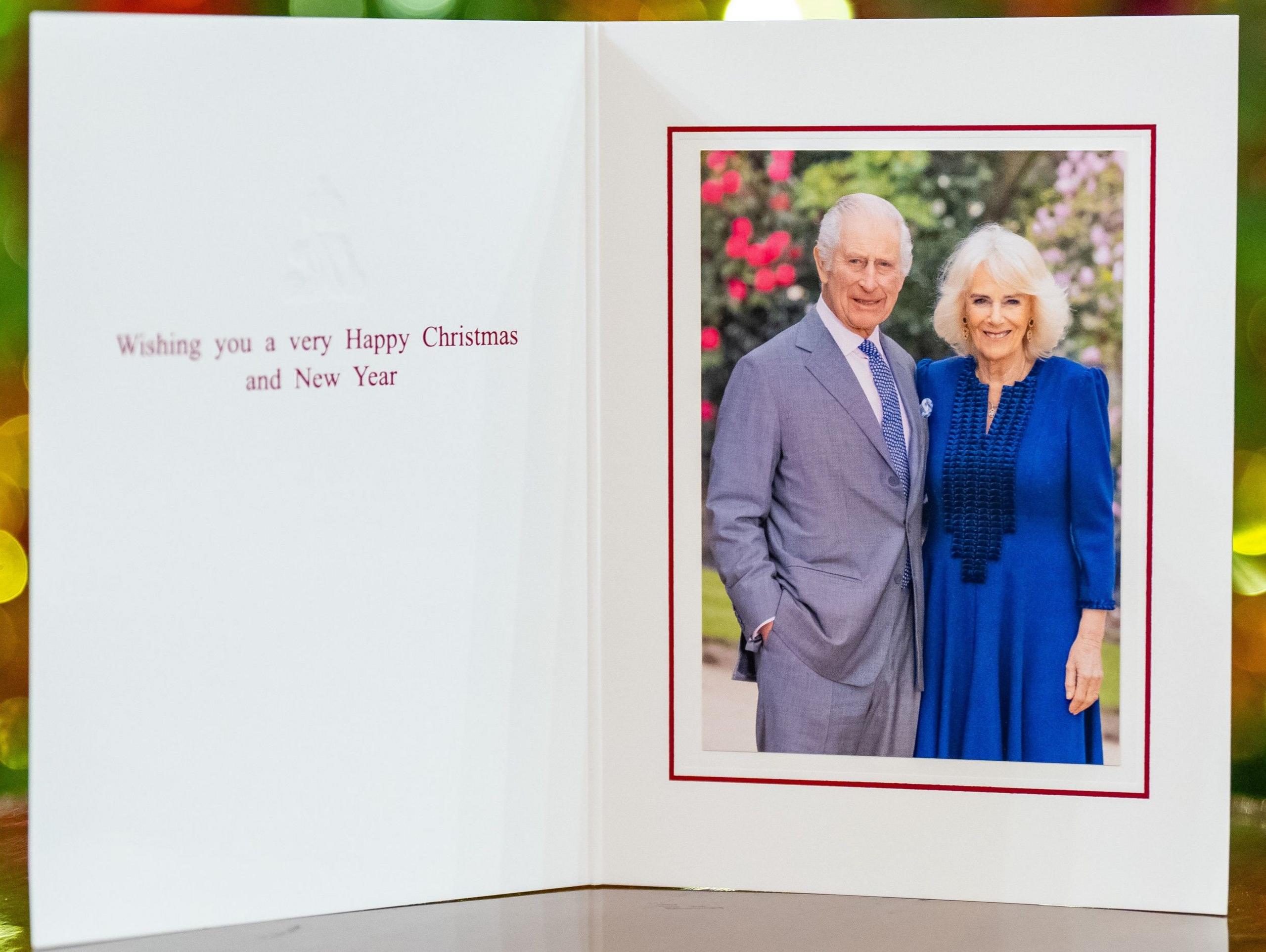 King and Queen standing side by side in photograph on card. The King - standing on the left - is wearing a grey suit and blue tie with his right hand tucked into his pocket, while the Queen wears a blue wool crepe dress. Card message reads: "Wishing you a very happy Christmas and New Year"