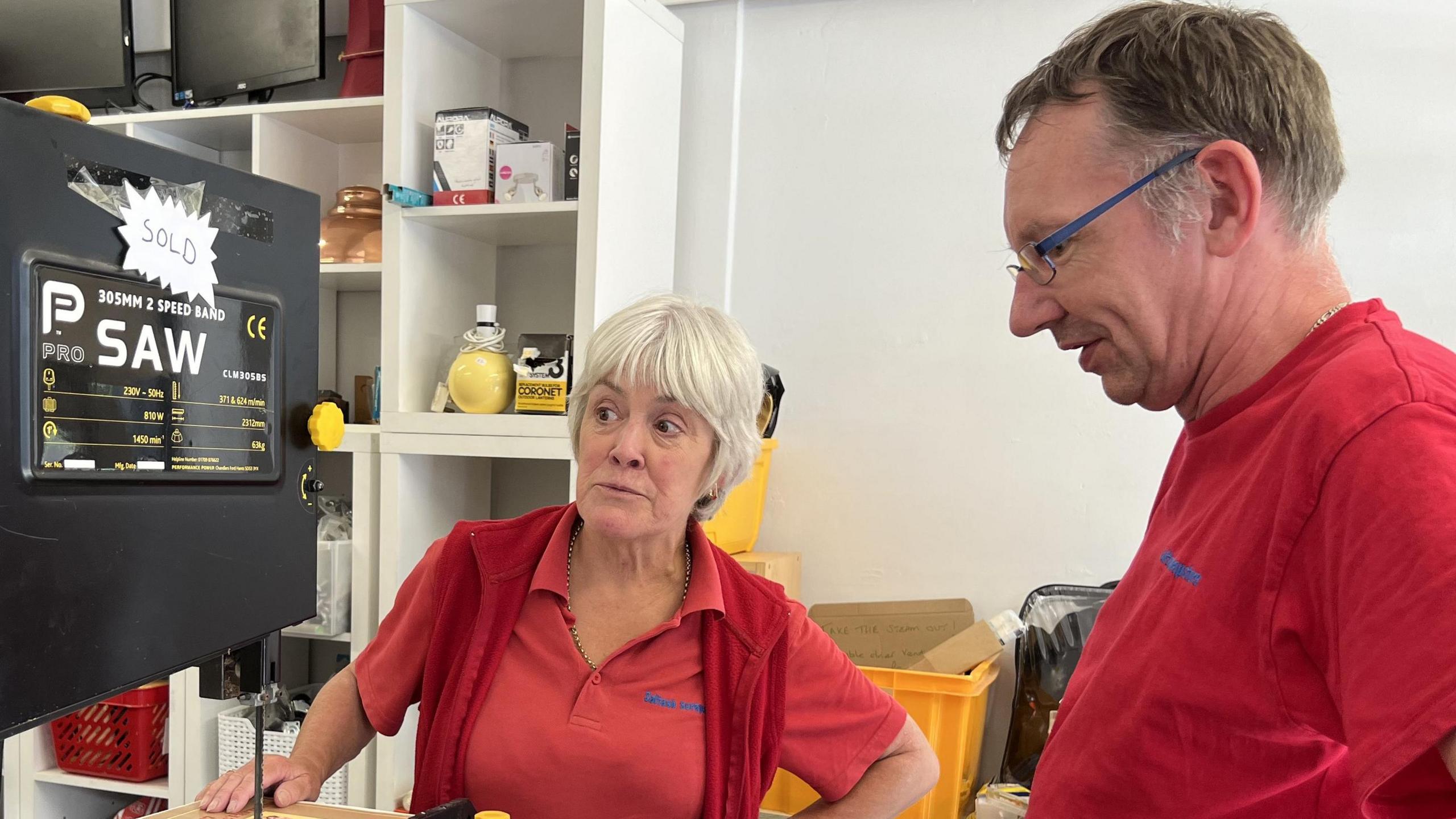 Two people wearing red T-shirts examine a large band saw