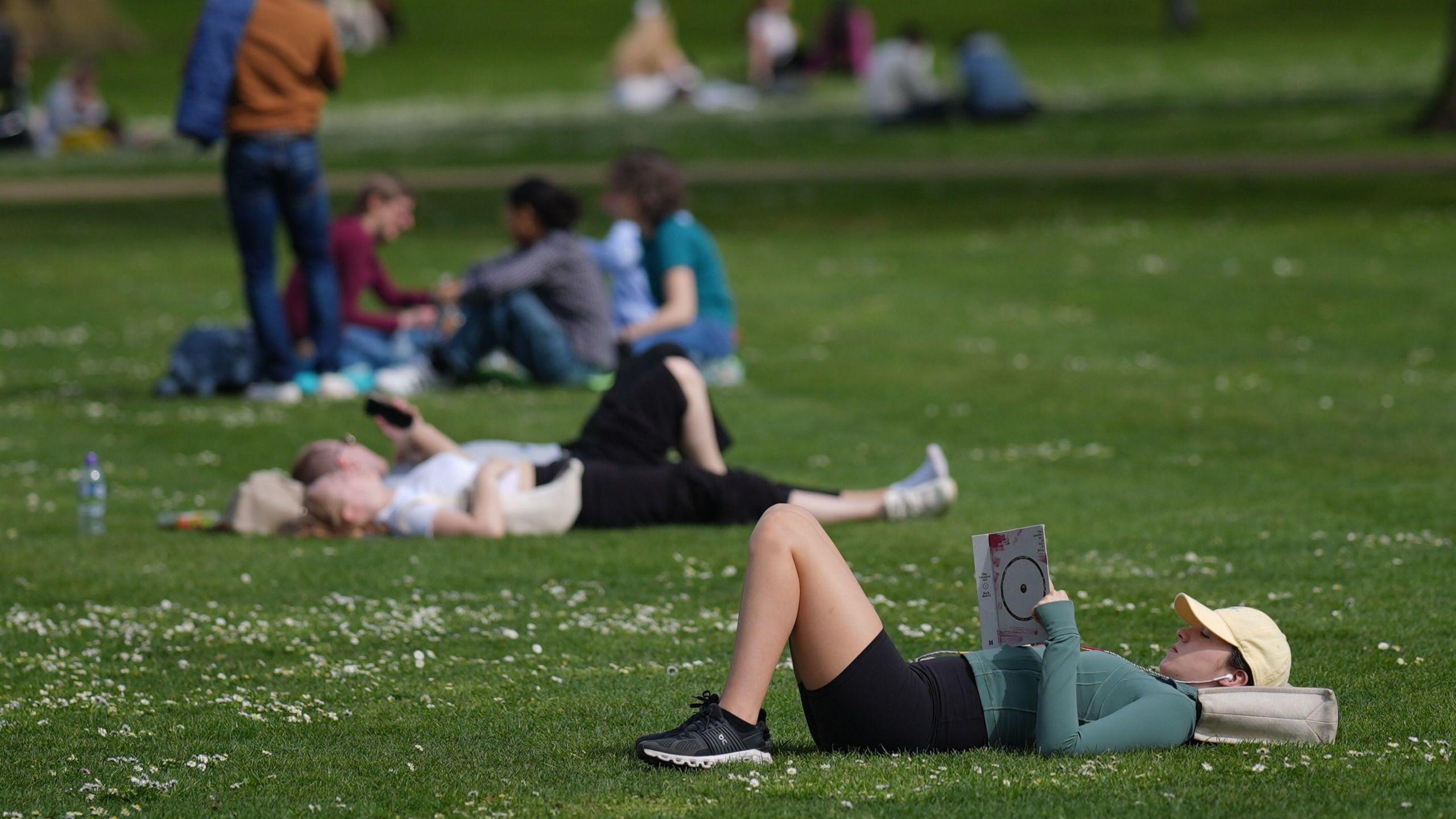 A woman sunbathes in a park during warm weather on 13 April