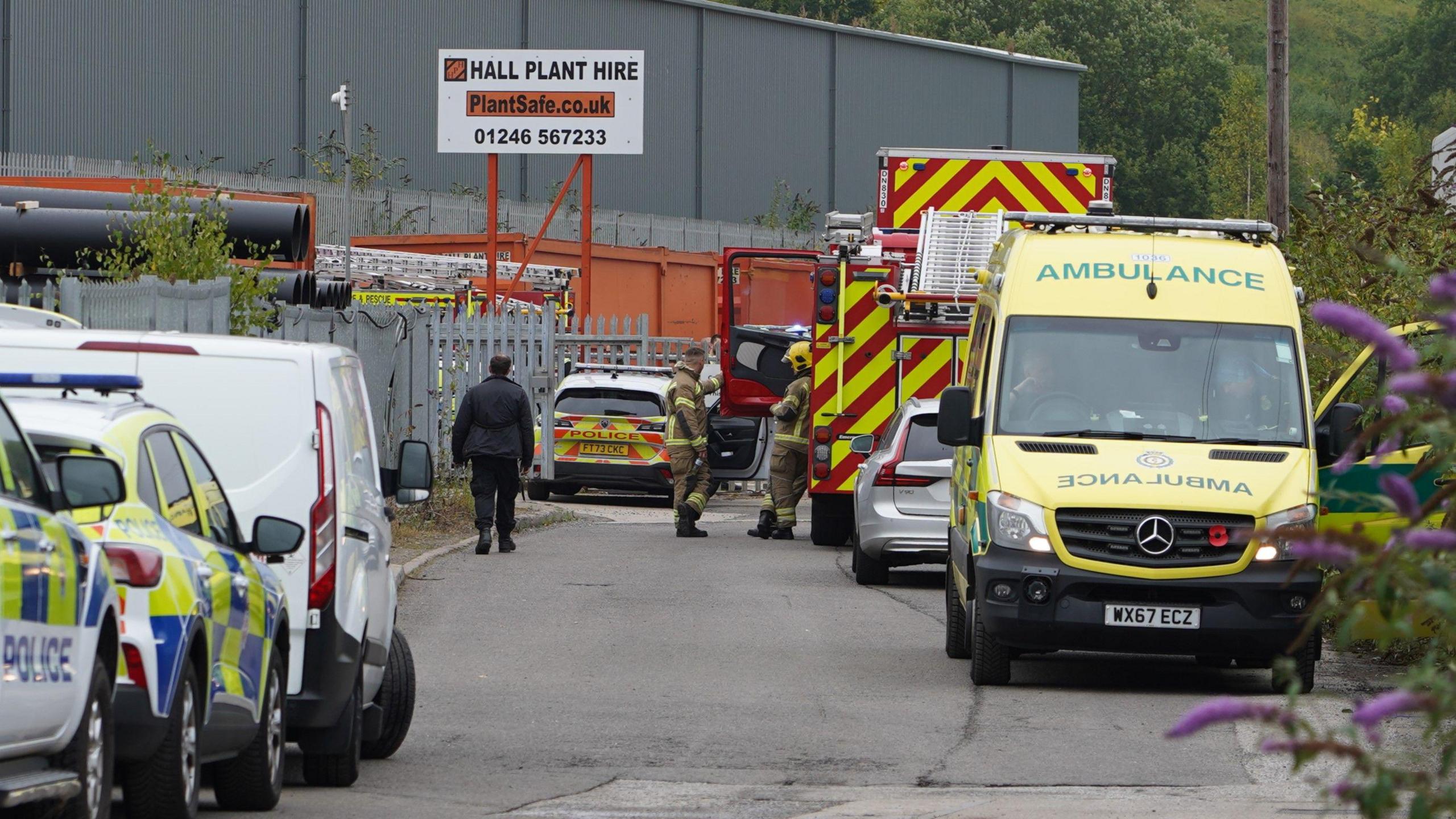 A number of emergency service vehicles parked in a narrow road leading to an industrial estate in Chesterfield. 