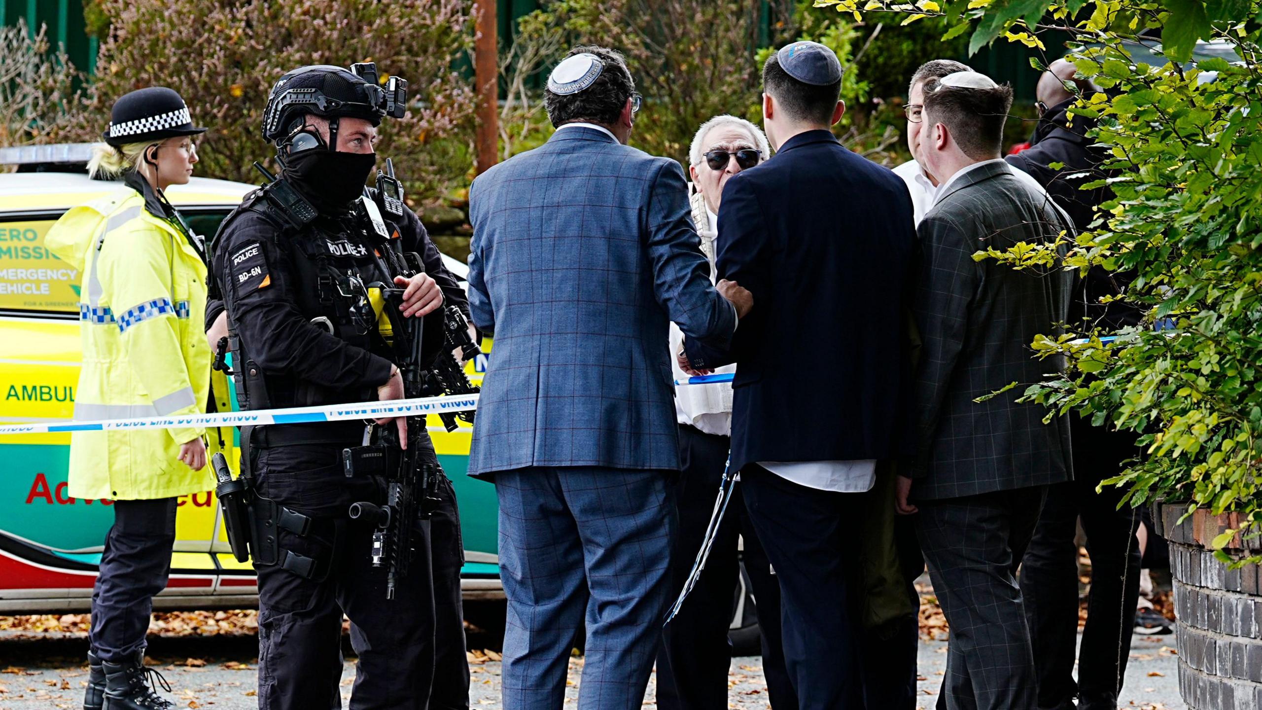 Five men talking to a police officer near the cordon. In the background is a police van