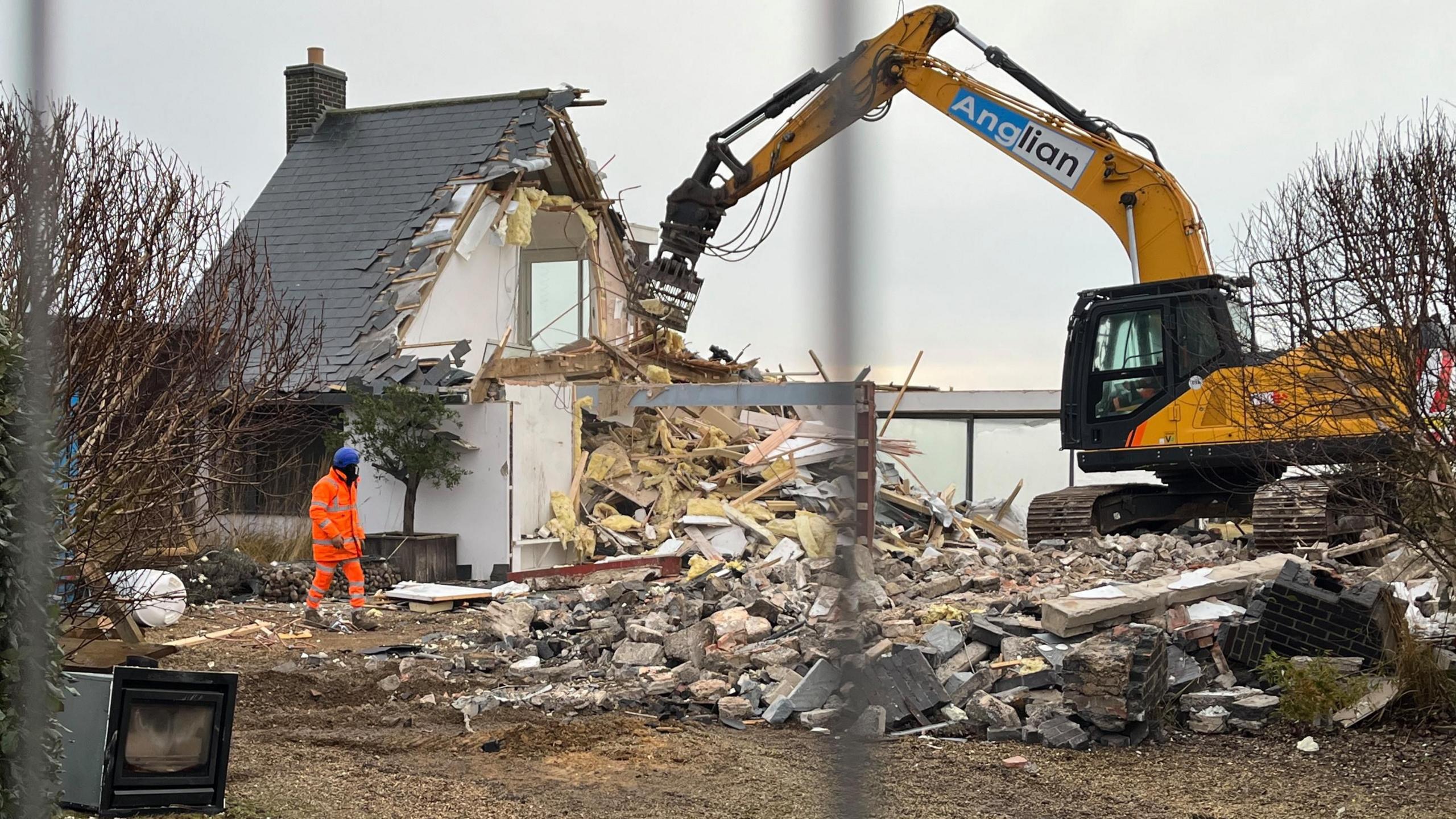A digger being used to demolish a house hanging on the edge of Thorpeness in Suffolk.