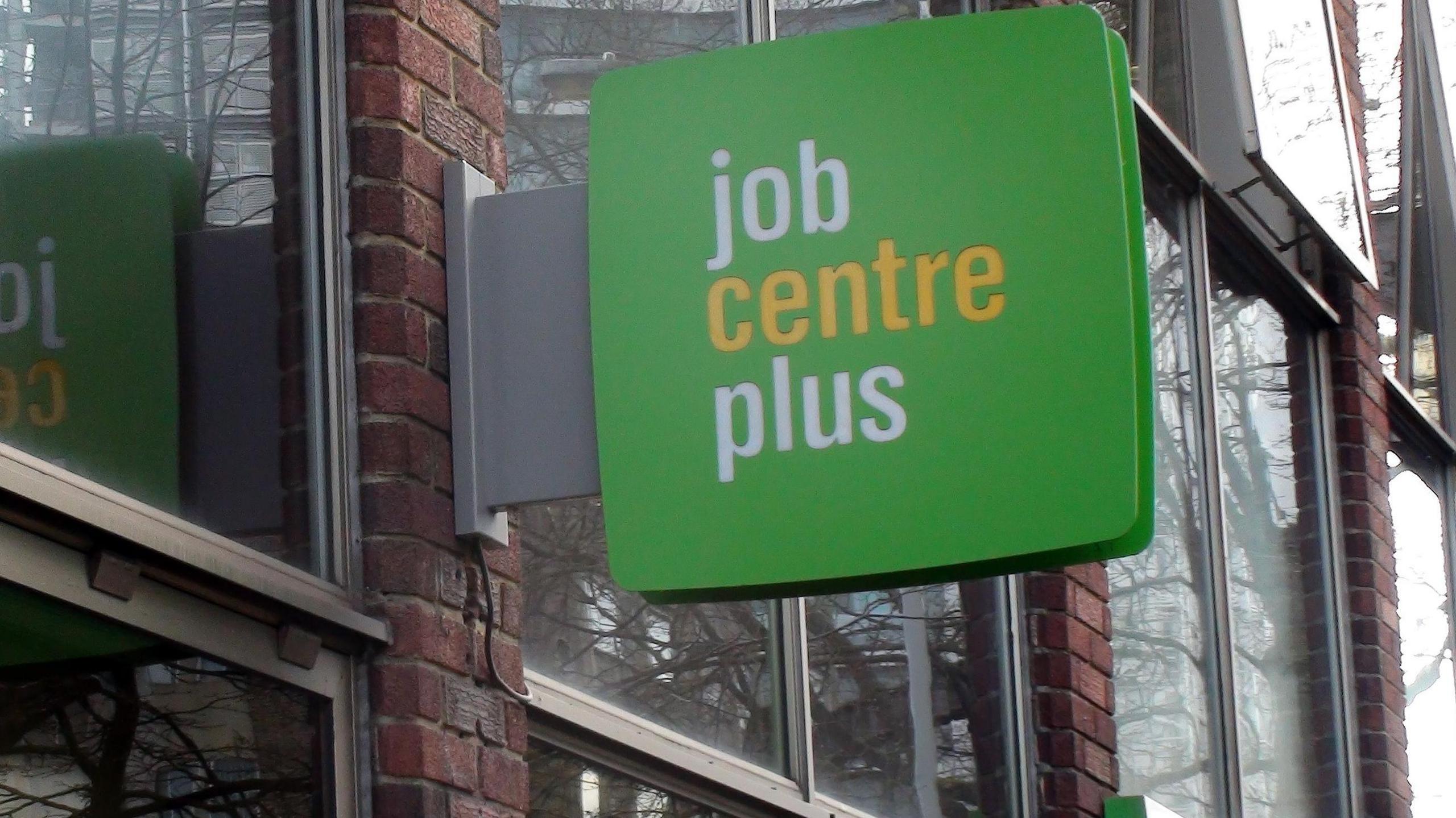 Jobcentre Plus sign on a building with a green background and writing in white and yellow