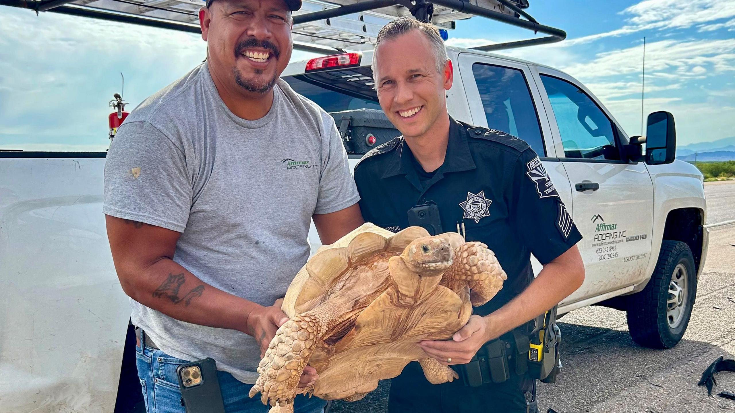 A state trooper and a motorist hold up a rescued tortoise