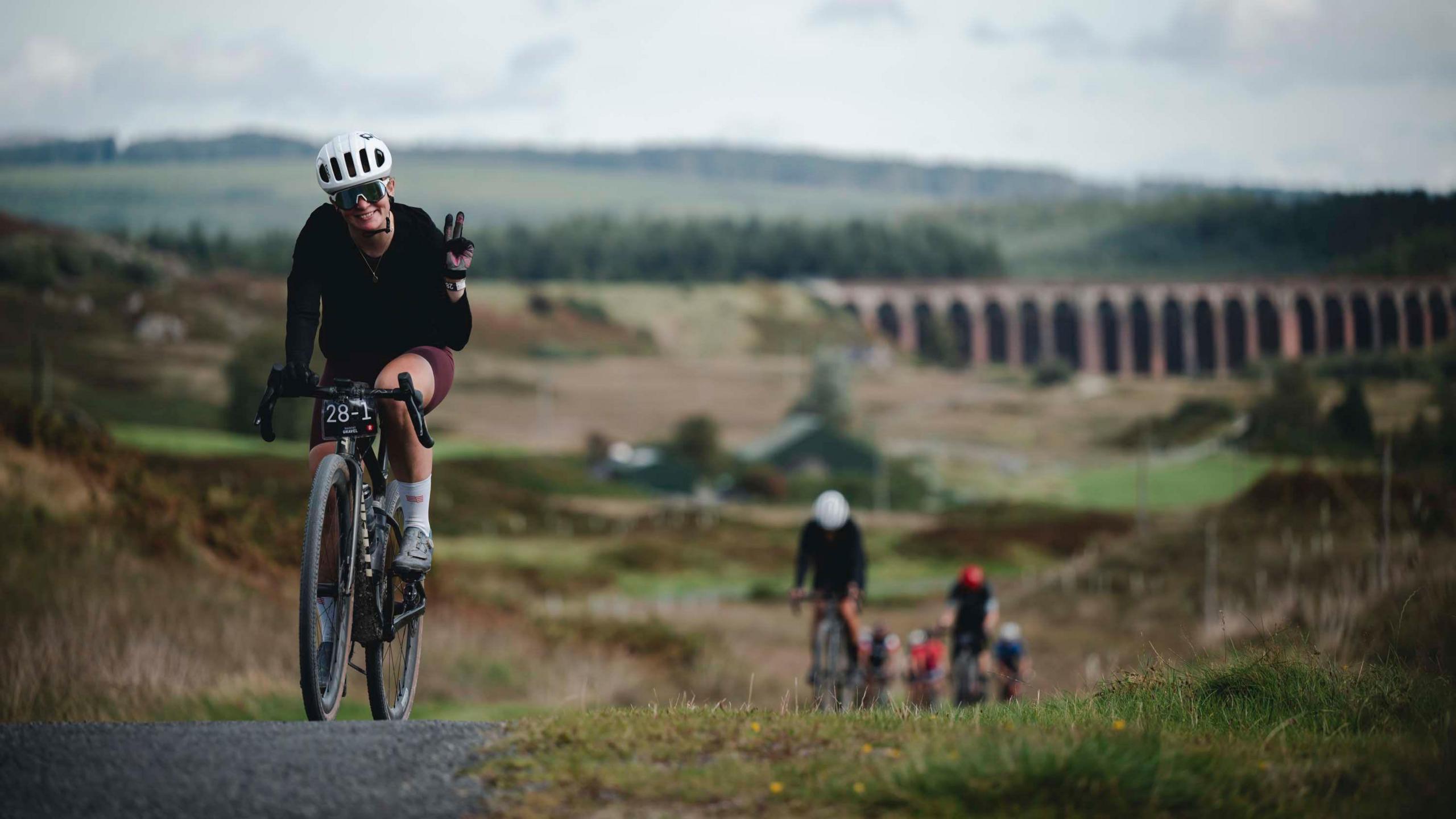 A cyclist reaches the crest of a hill and waves as others struggle on behind her through the Galloway Forest Park