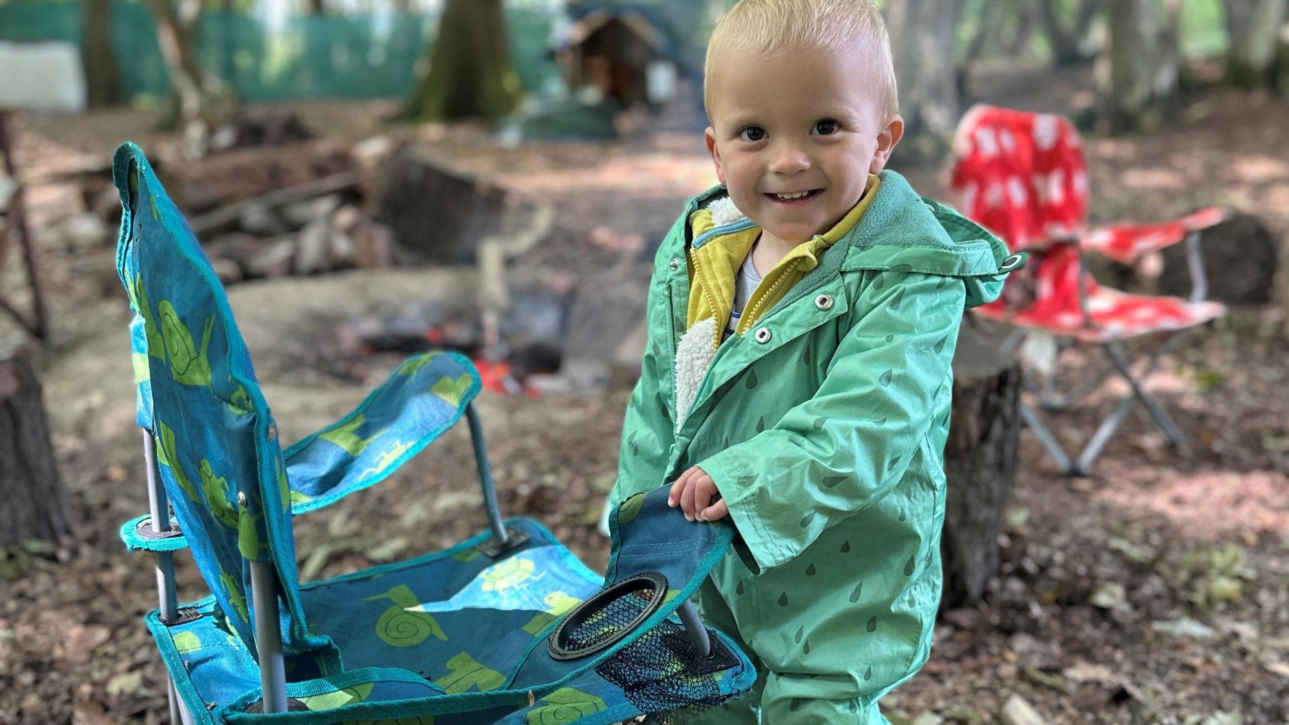 Woody wearing a viridian coat and standing next to a camping chair.
