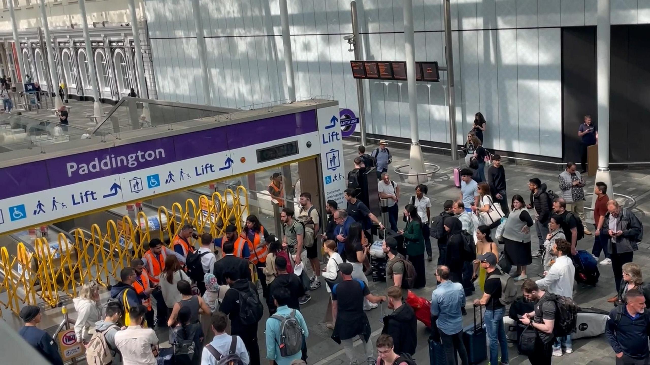 Crowd of people with luggage entering Paddington station via the Elizabeth line entrance.