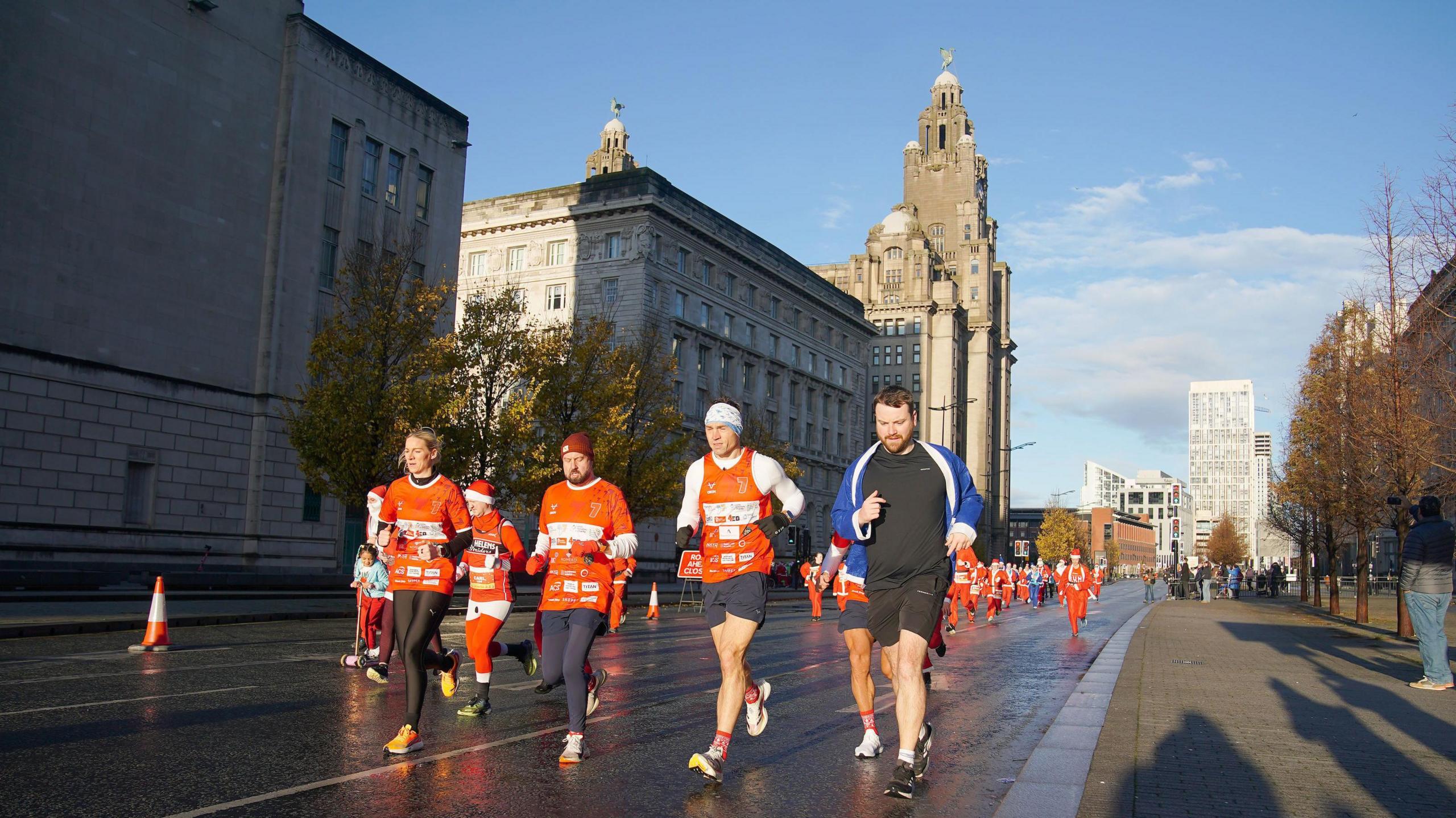 Kevin Sinfield running with three support runners with a sunlit Liver Building in the background