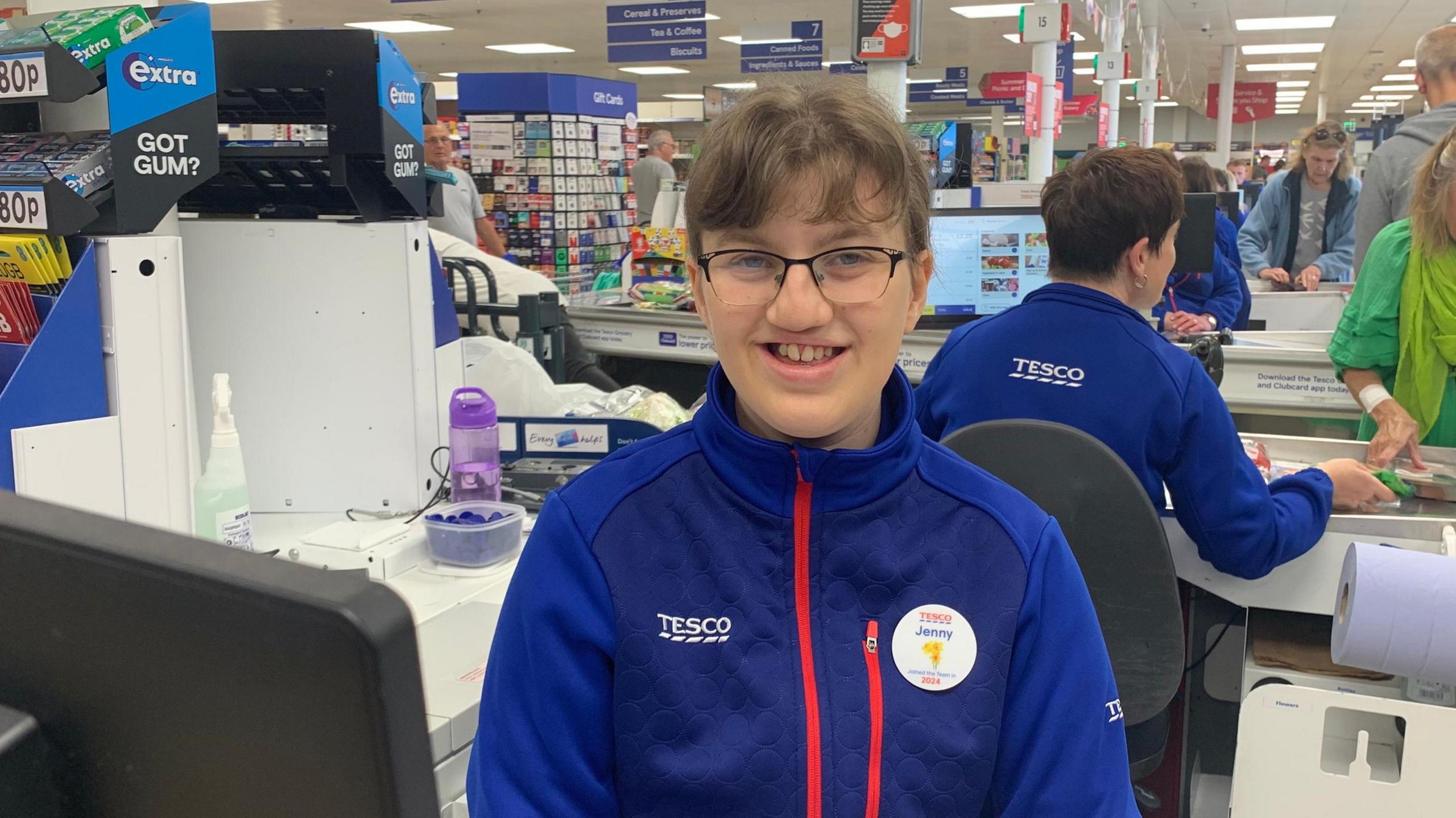 Jenny Beesley sitting behind a checkout in Tesco in her uniform