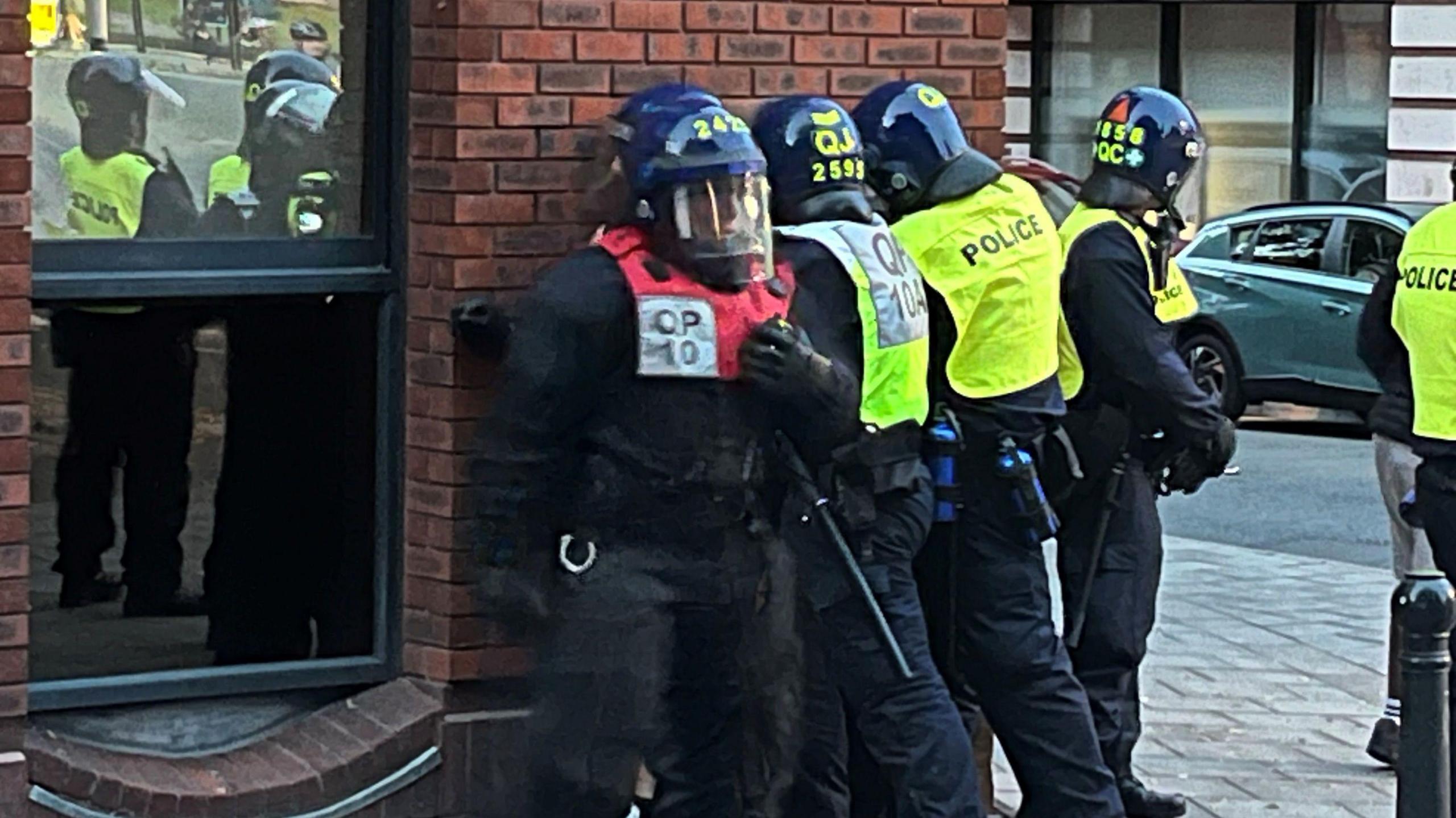 Four police officers in riot gear standing against a wall outside