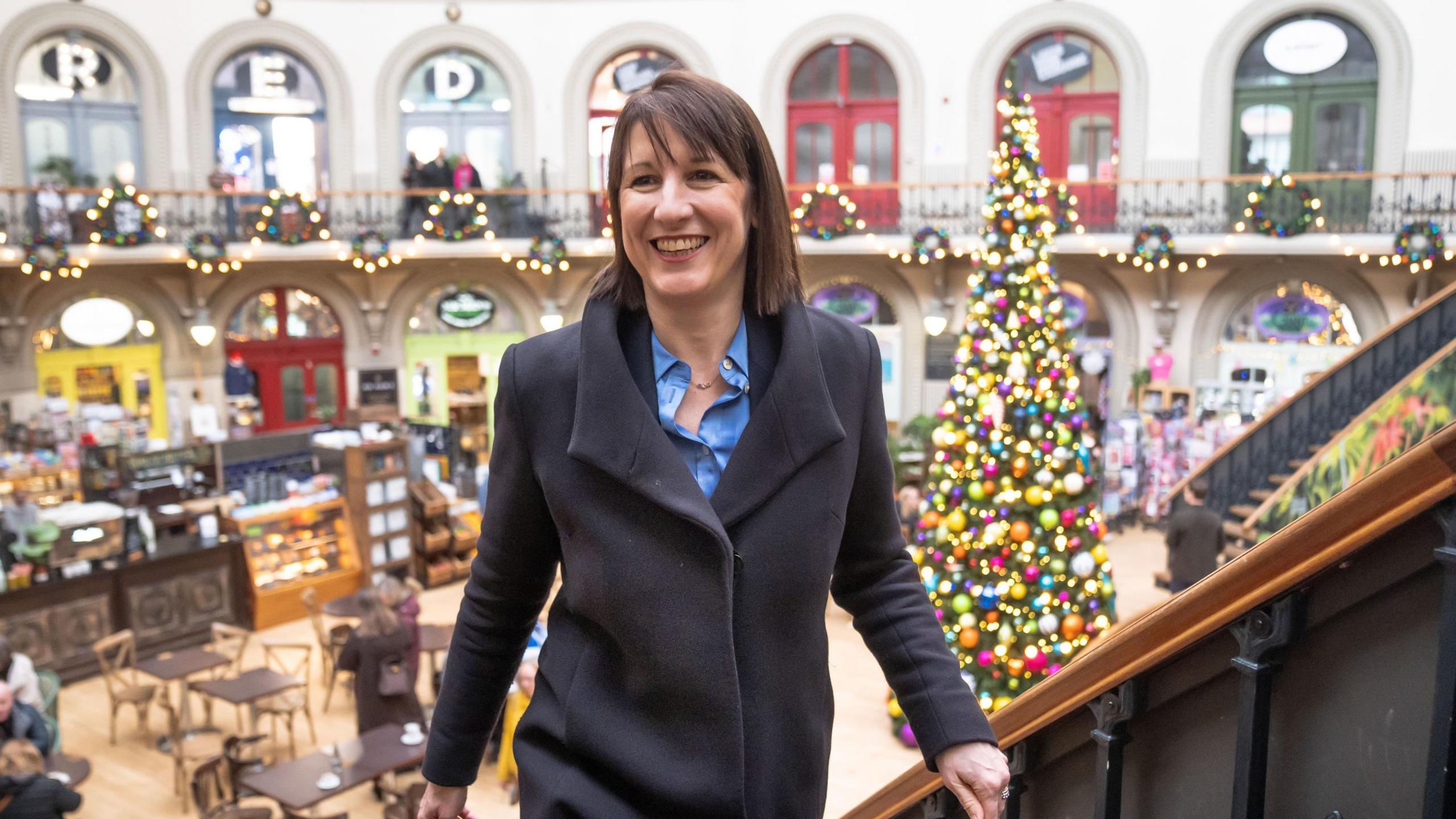 Chancellor Rachel Reeves standing on a balcony in the Corn Exchange, leeds with Christmas decorations in the background.