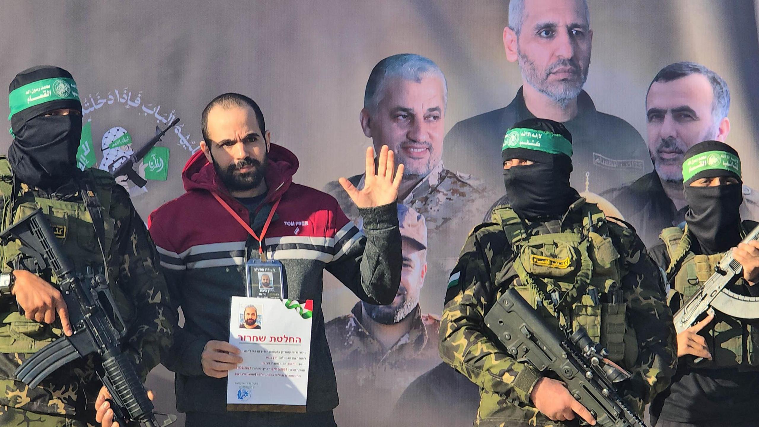 Yarden Bibas, a hostage held in Gaza, waves from a stage in Khan Younis while flanked by two armed and masked Hamas fighters.