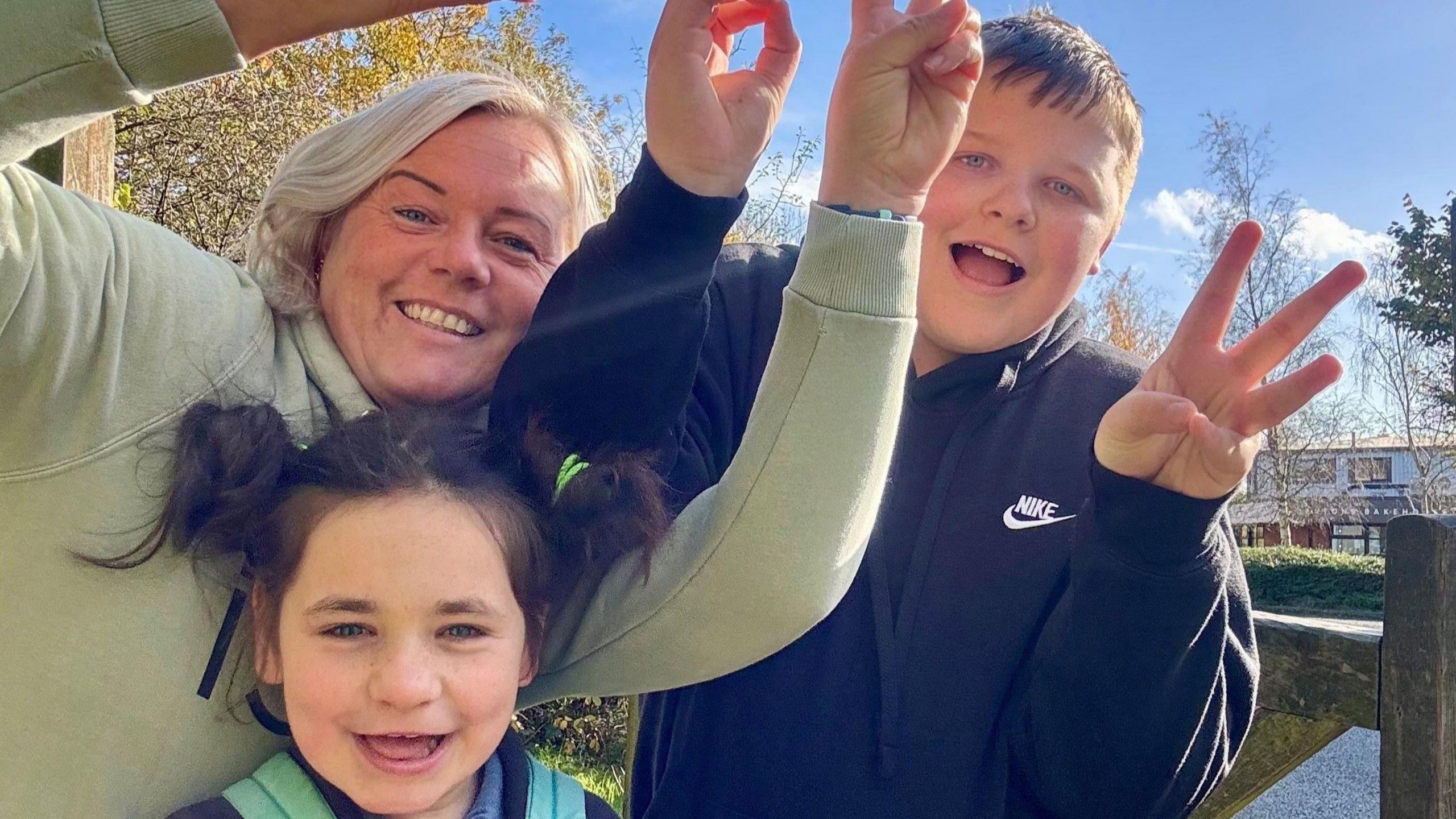 Nathalie is pictured with her son and her daughter Penny. They are looking into the camera smiling and holding up peace signs. 