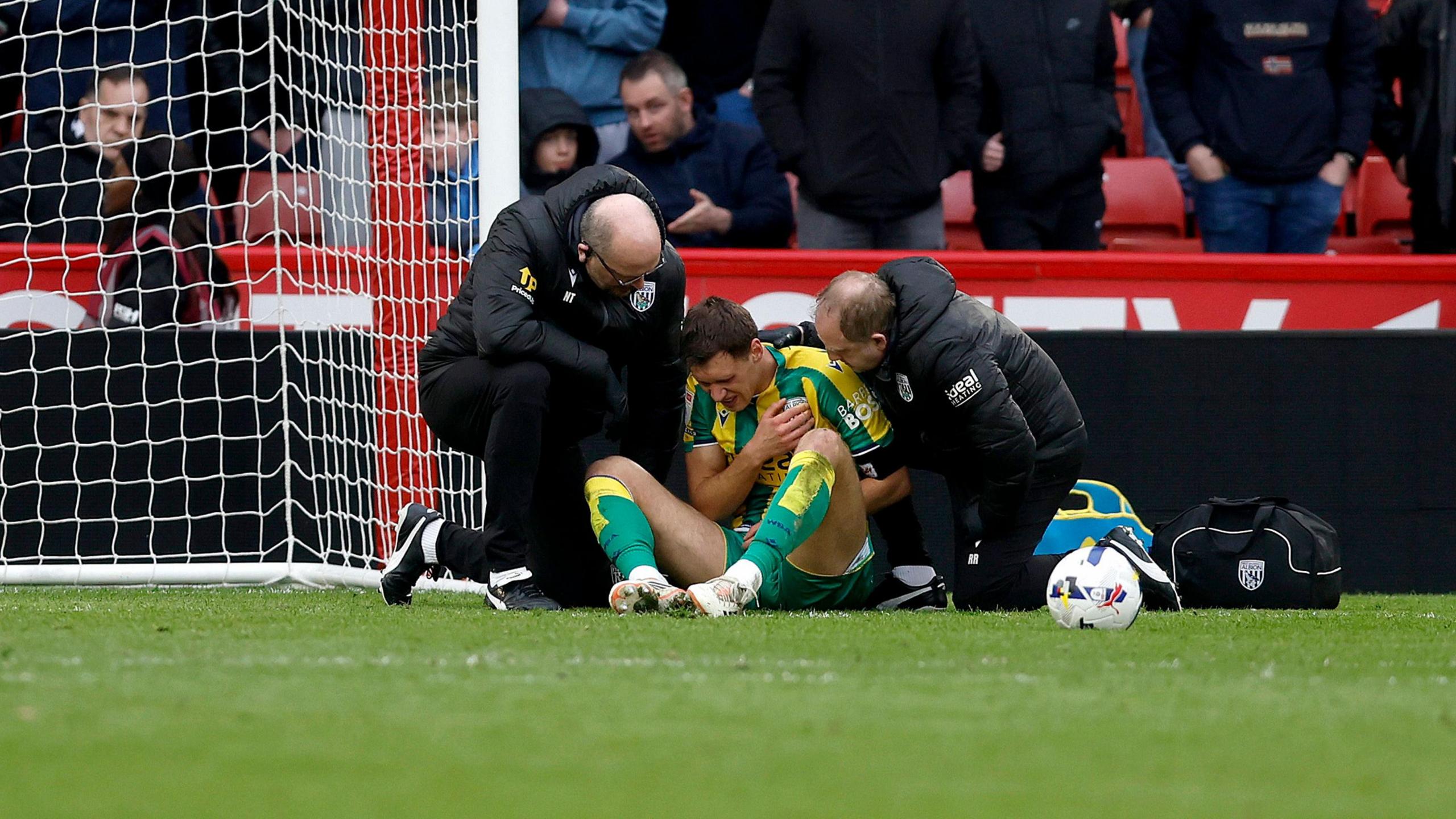 Krystian Bielik holding his shoulder and grimacing as he is attended to by medical staff at West Bromwich Albion's game against Sheffield United