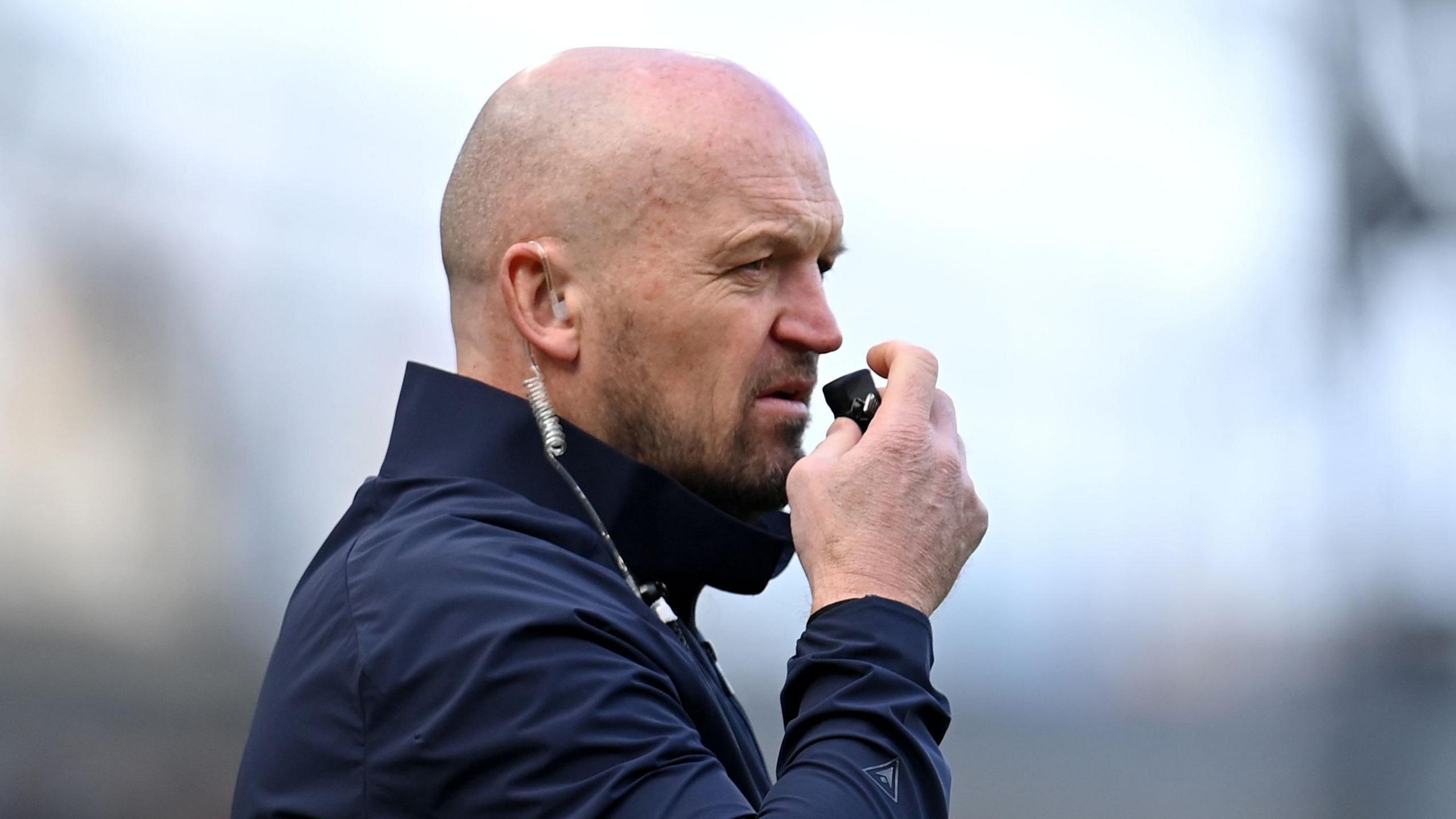 Gregor Townsend speaking into a mouthpiece while he is wearing an earpiece with wiring hanging down