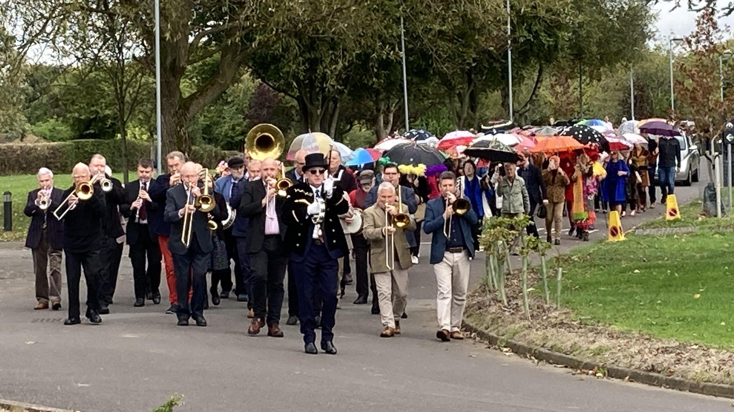 Mourners dressed in bright outfits and playing instruments walk towards a crematorium during a funeral in Bristol. Some are also holding brightly-coloured umbrellas