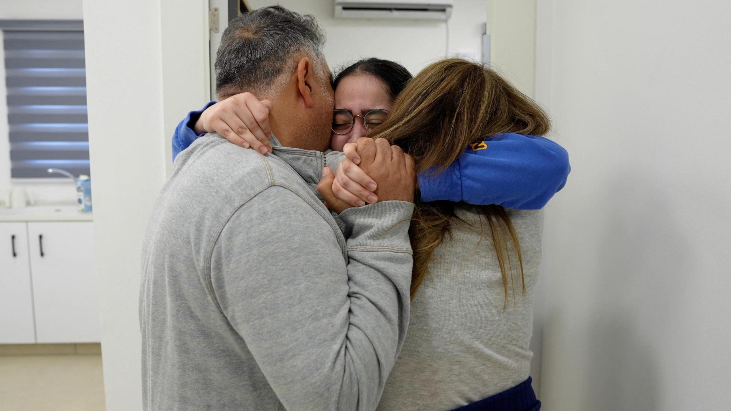 Liri Albag tightly embracing her parents who are wearing grey tops.