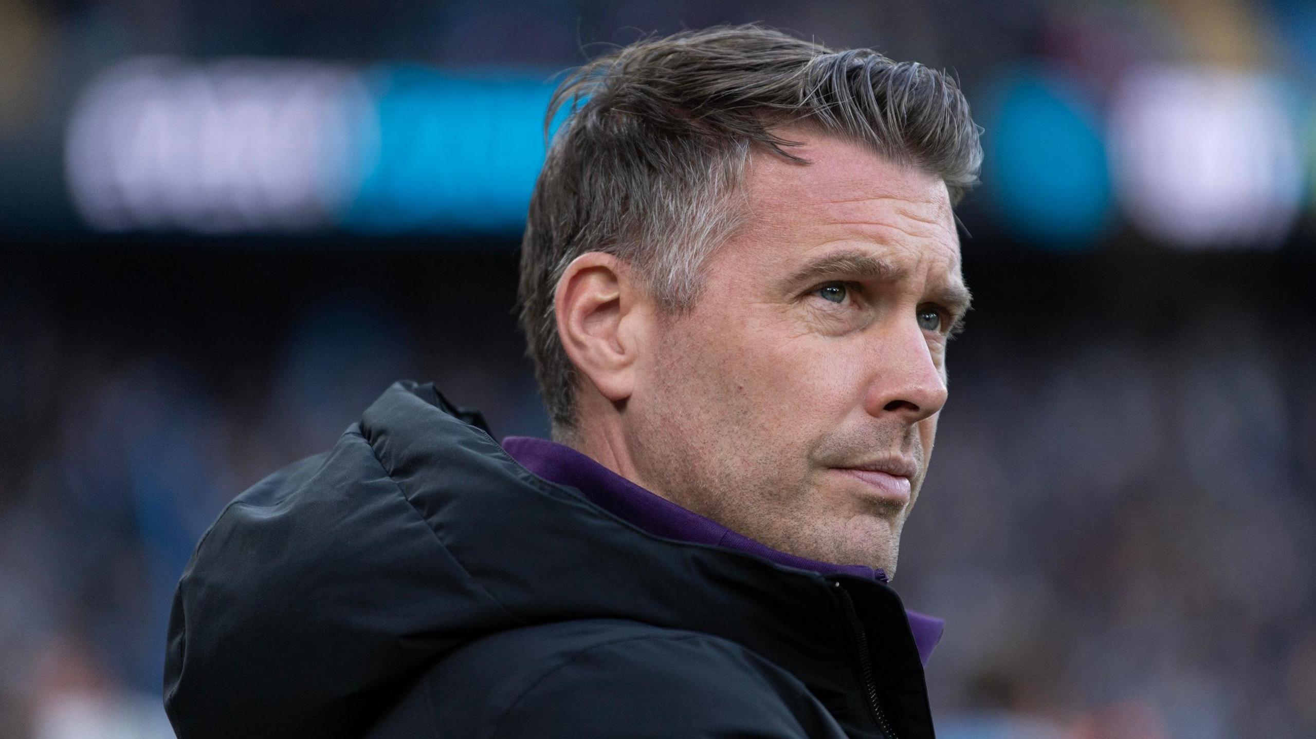 A close up of Rob Edwards, wearing a hooded black jacket, watching Wolves play Manchester City at the Etihad in January