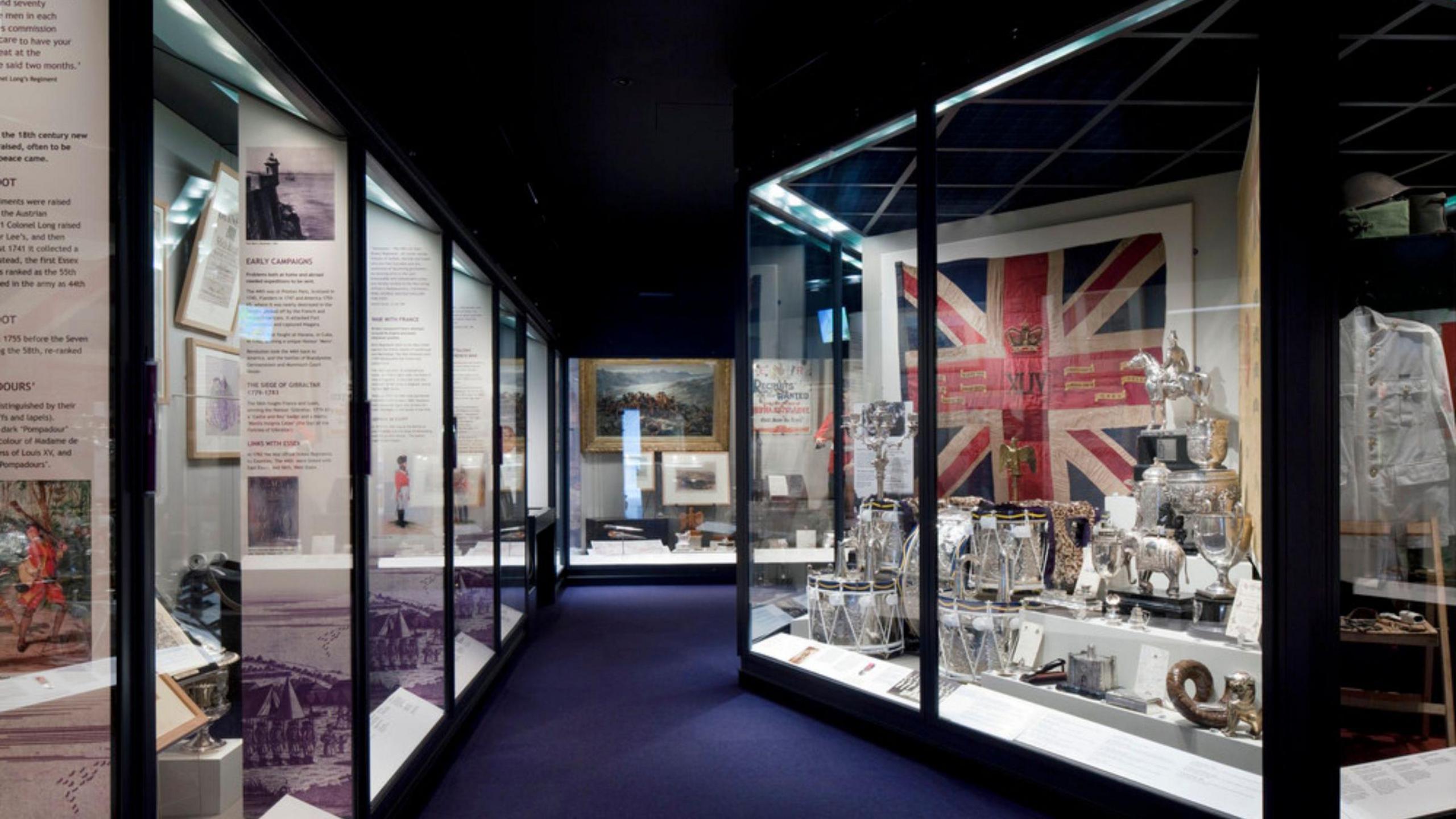 A wide shot of a room with some artefacts behind glass including a large Union Jack flag