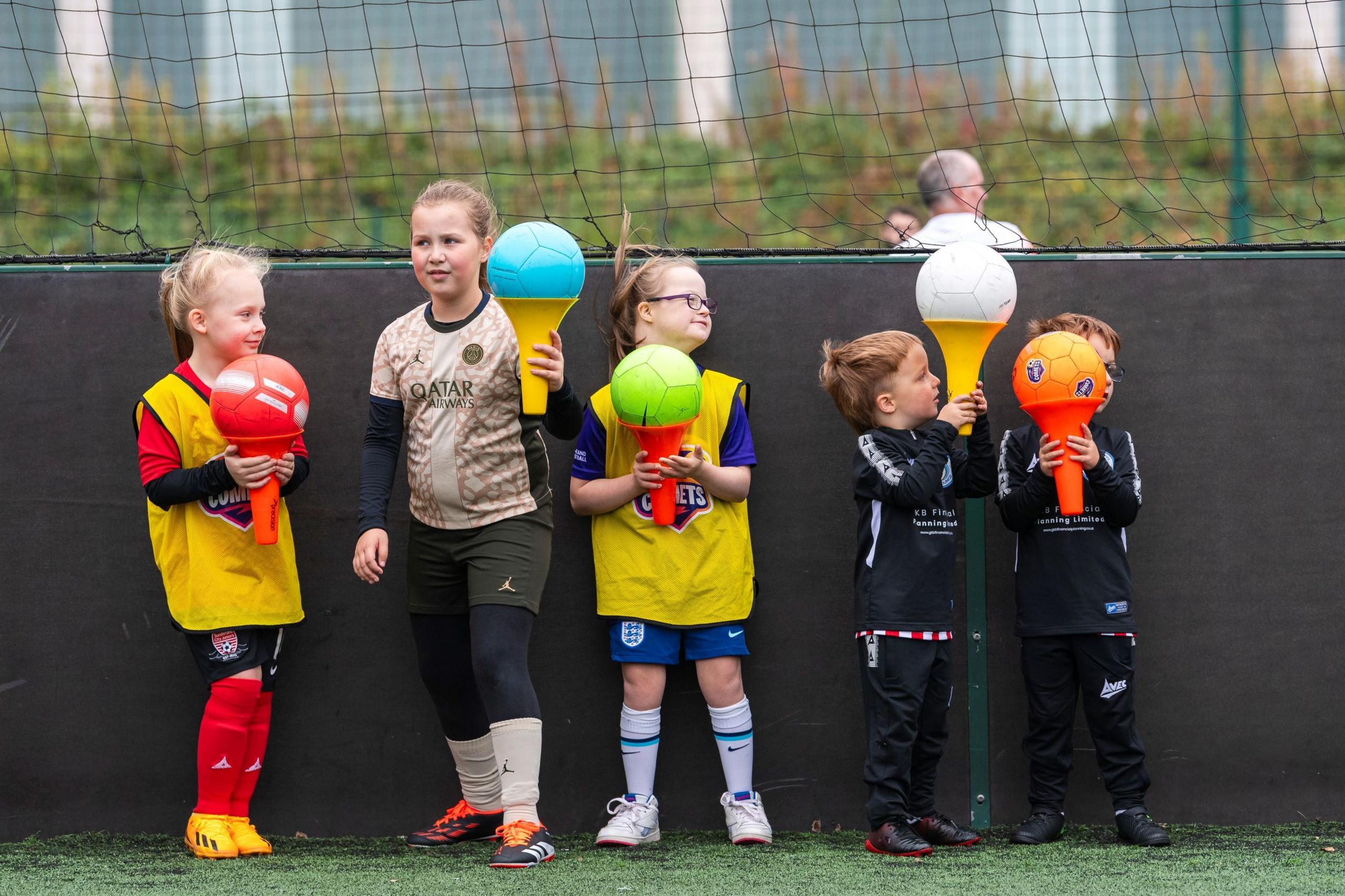 Five kids hold footballs in plastic cones during a Comets session. 