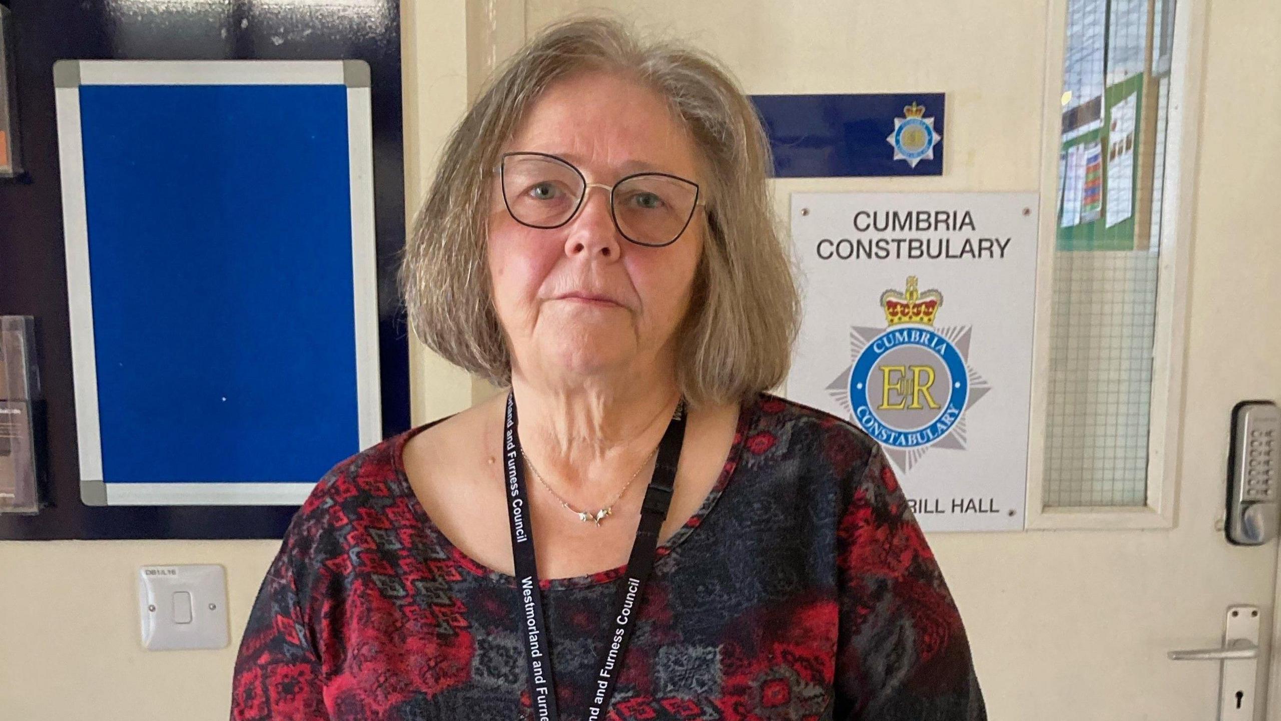 A woman with a grey-brown bob and glasses with a glum expression.