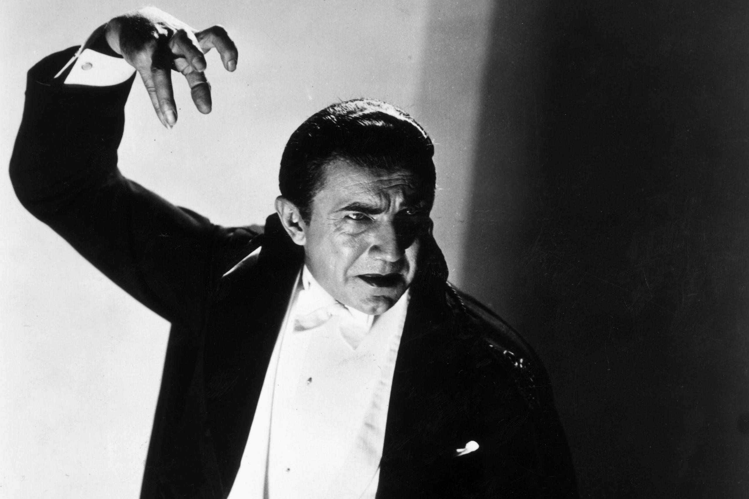 Black and white photo of Bela Lugosi as Dracula - in a black dinner suit  looking down and his right arm up - with his hand in a claw