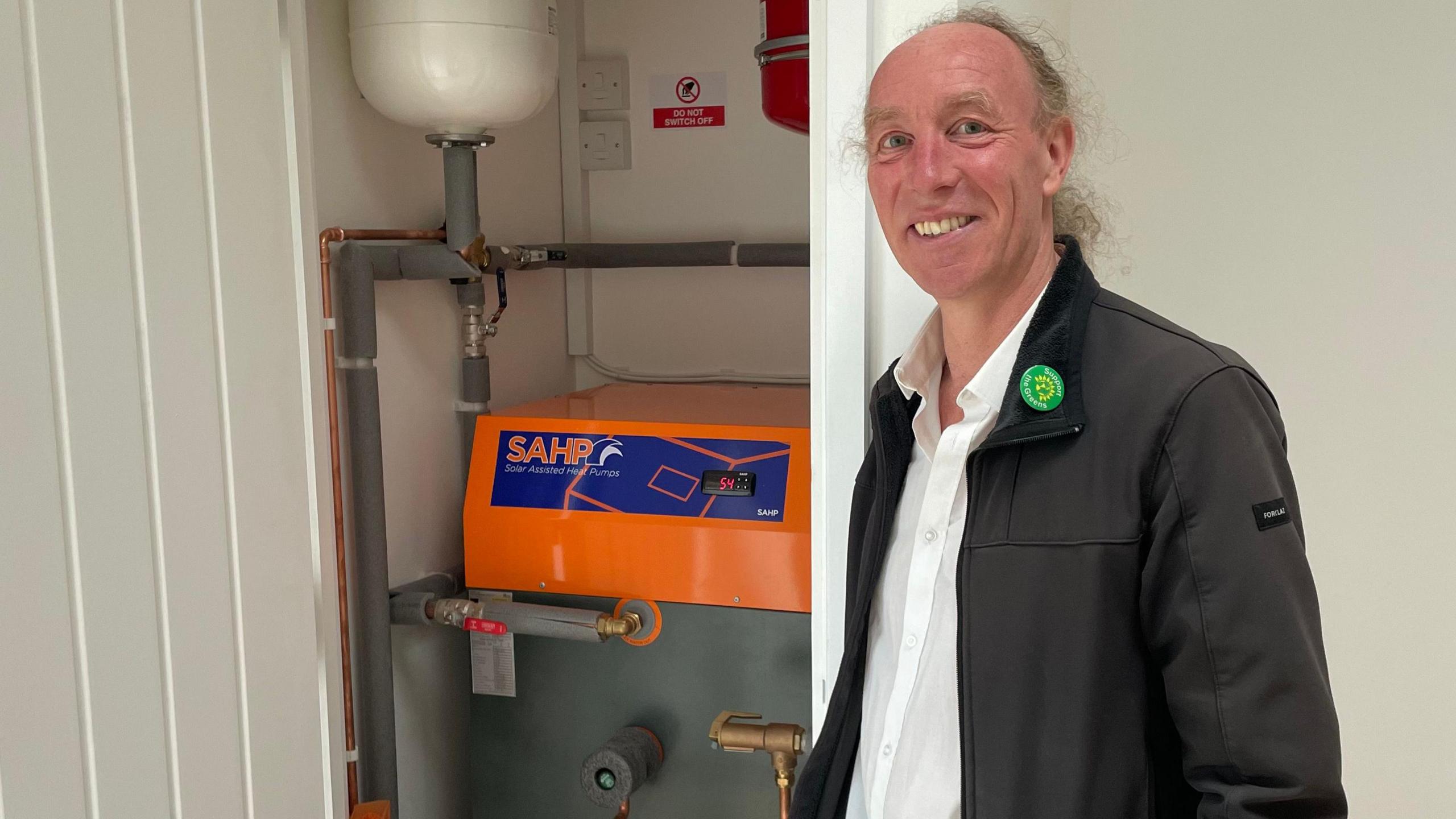 Cllr Johnson, a middle-aged man, stood next to the energy-efficient heat pump in a cupboard.