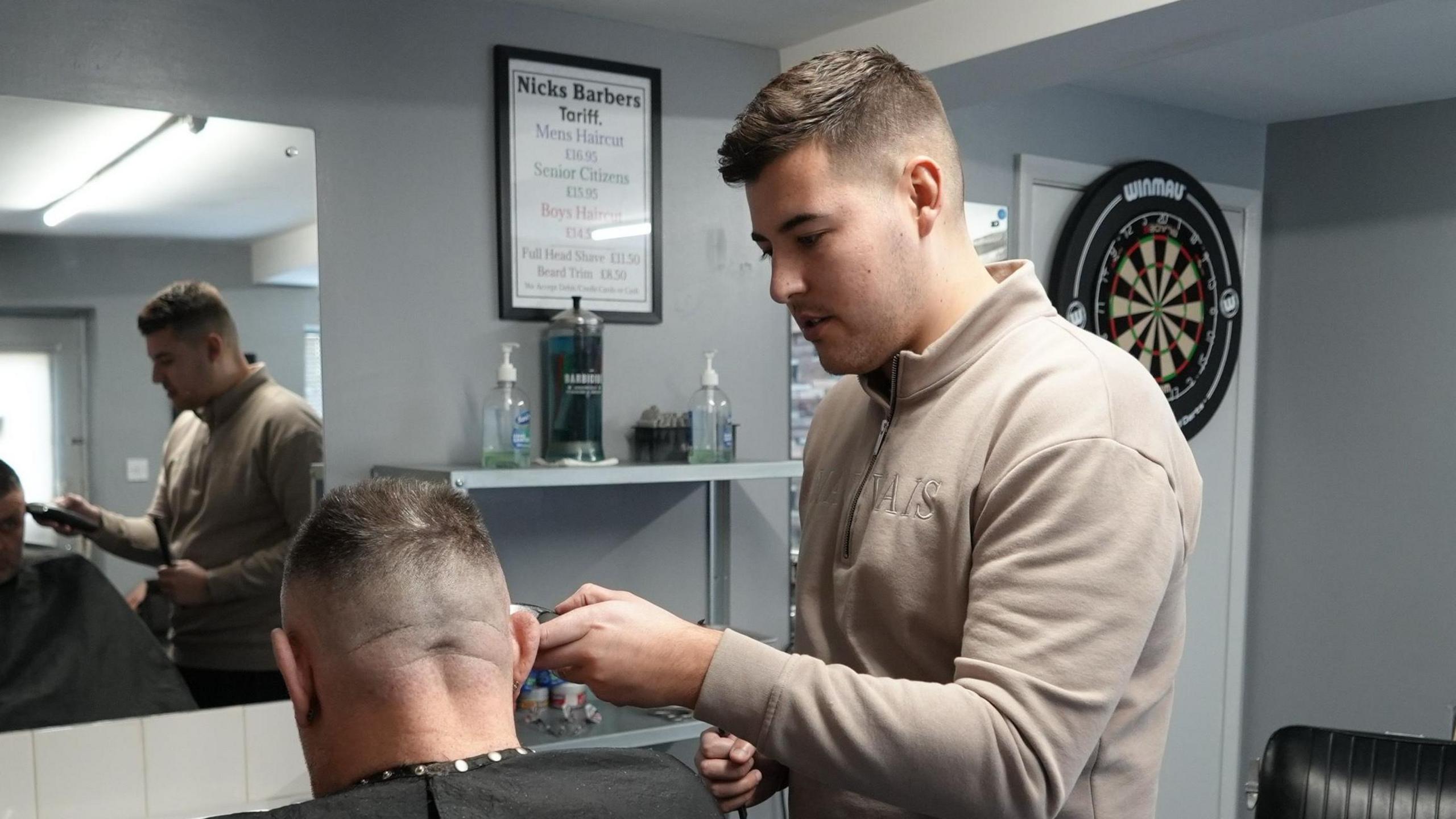 Meikle is pictured giving a gentleman in a chair a haircut. He is holding a pair of clippers to the man's head.