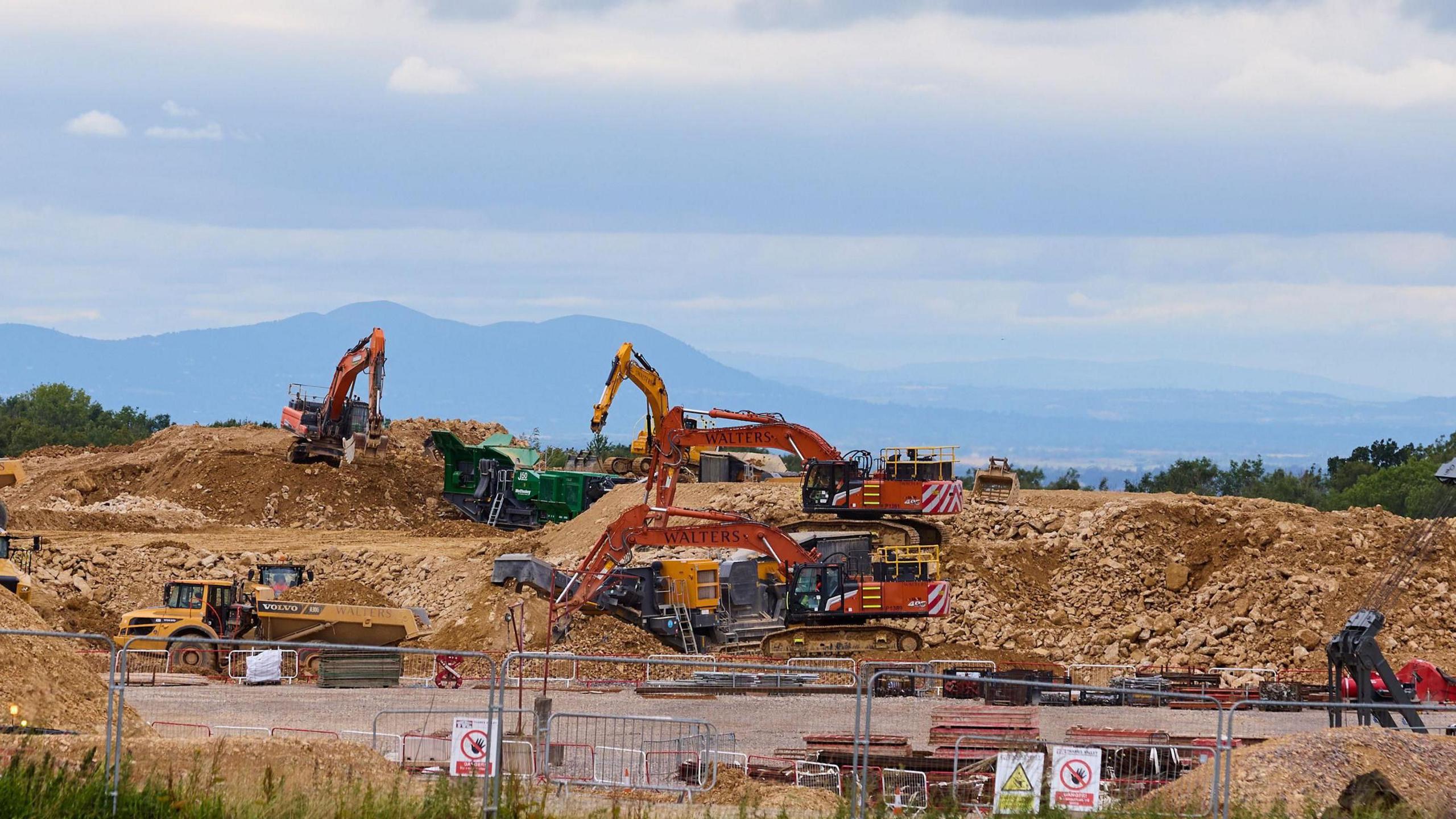 Diggers and trucks working on embankments of brown-coloured rocks.