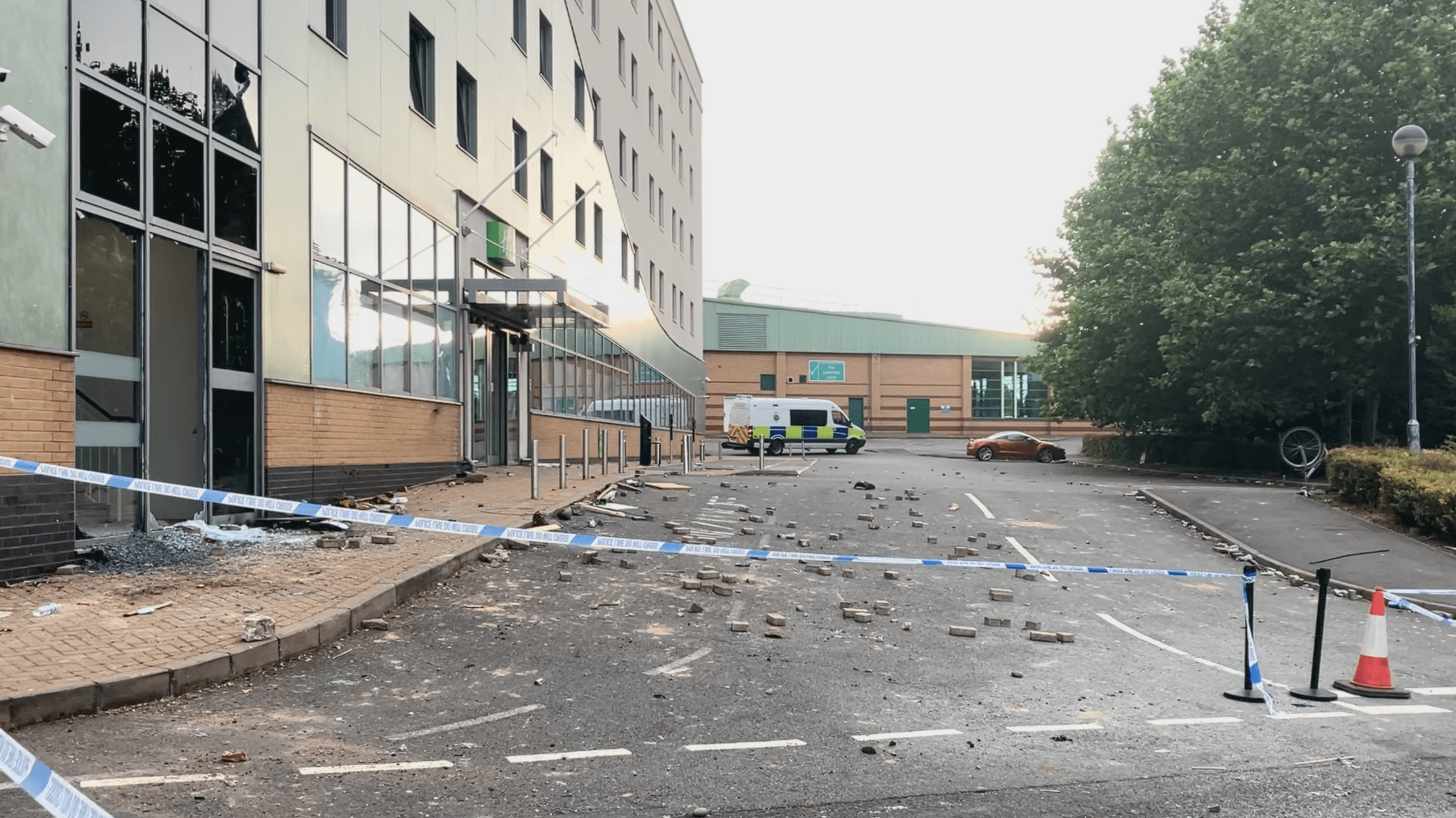 Rubble scattered on the pavement outside the hotel. A police cordon is in place and a police van is parked up outside the hotel