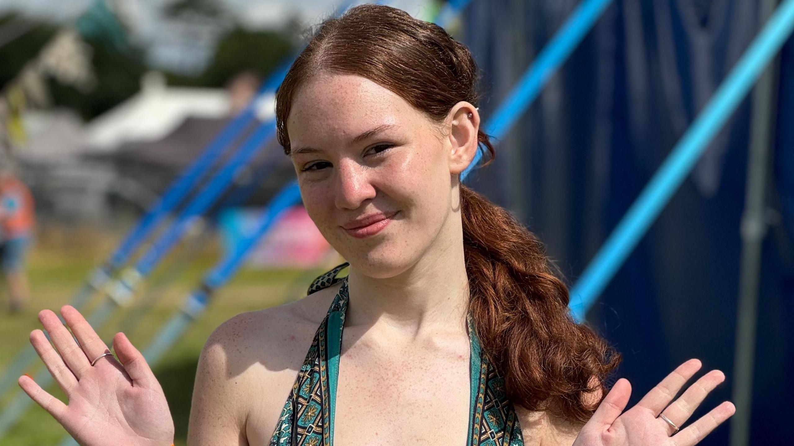 Lotte Cummins is wearing a green halter neck top and smiling at the camera. Her hands are waving out to the side.