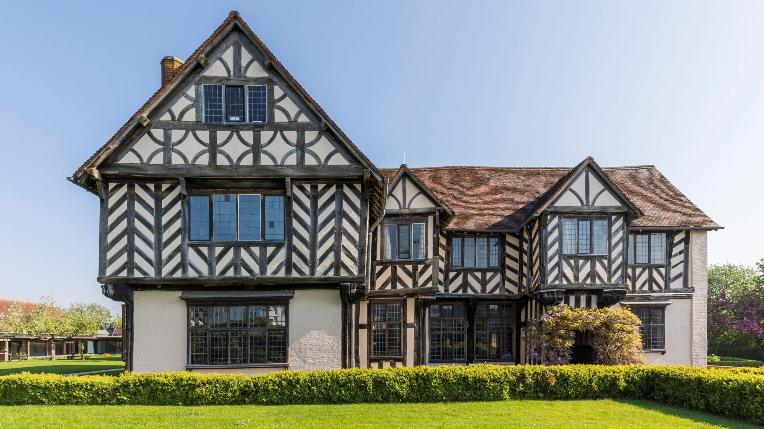 A large white house with black beams in decorative patterns on it. There is a lawn in front of the house.