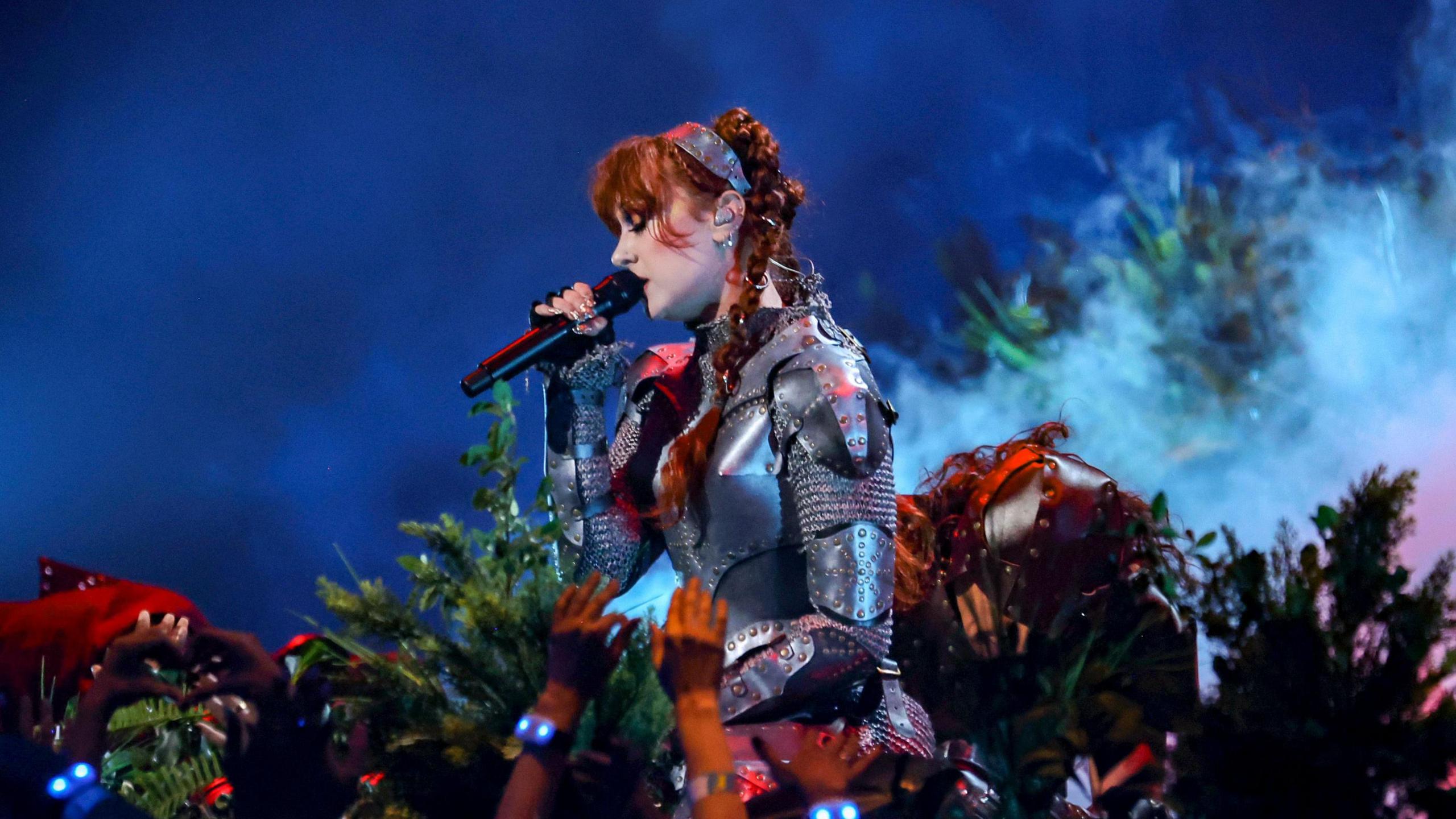 Singer Chappell Roan dressed as a night, in front of flowers on stage, performing for a crowd at the VMAs