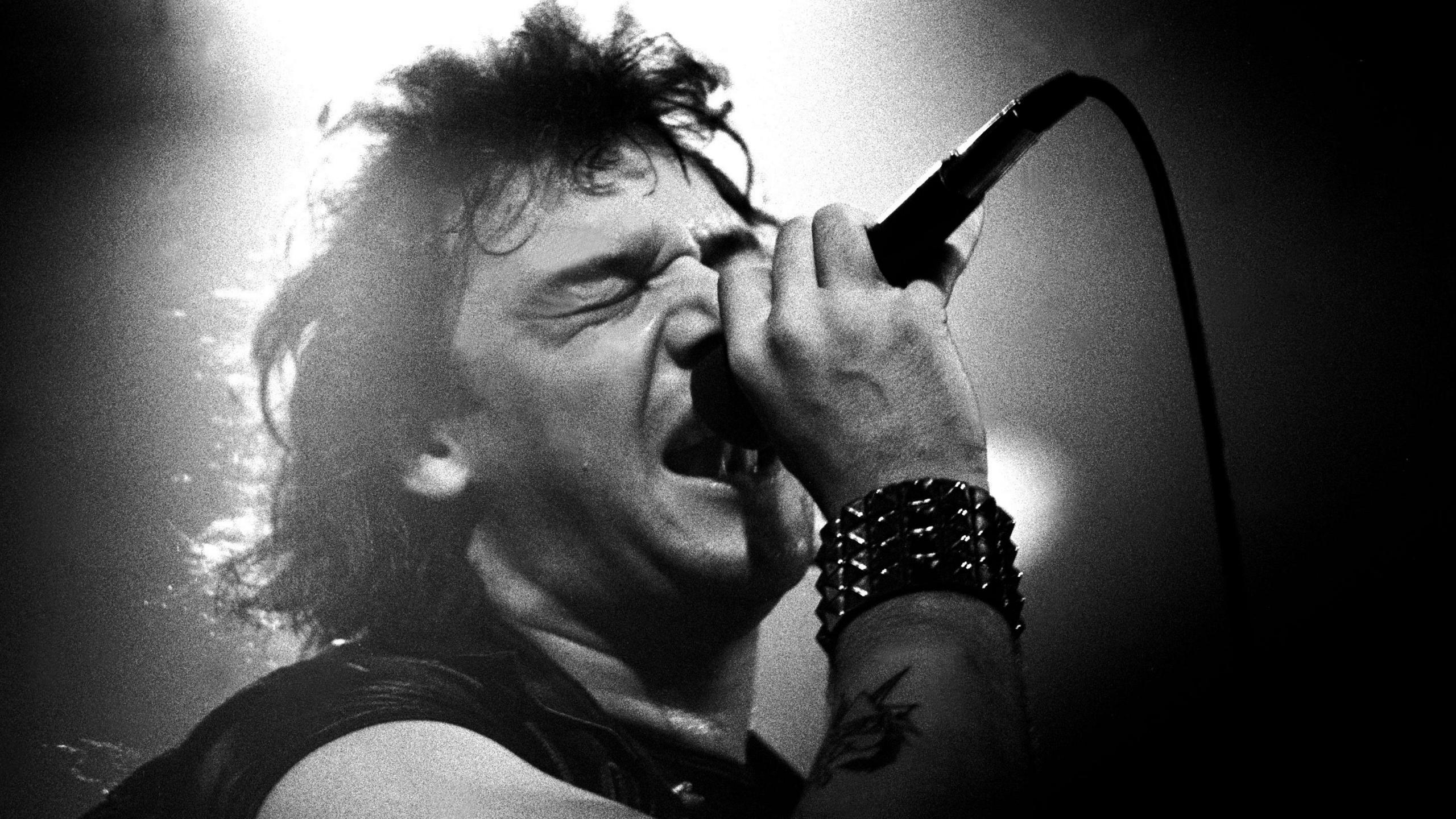 A black and white photograph of Paul Di'Anno performing with Iron Maiden in 1981.