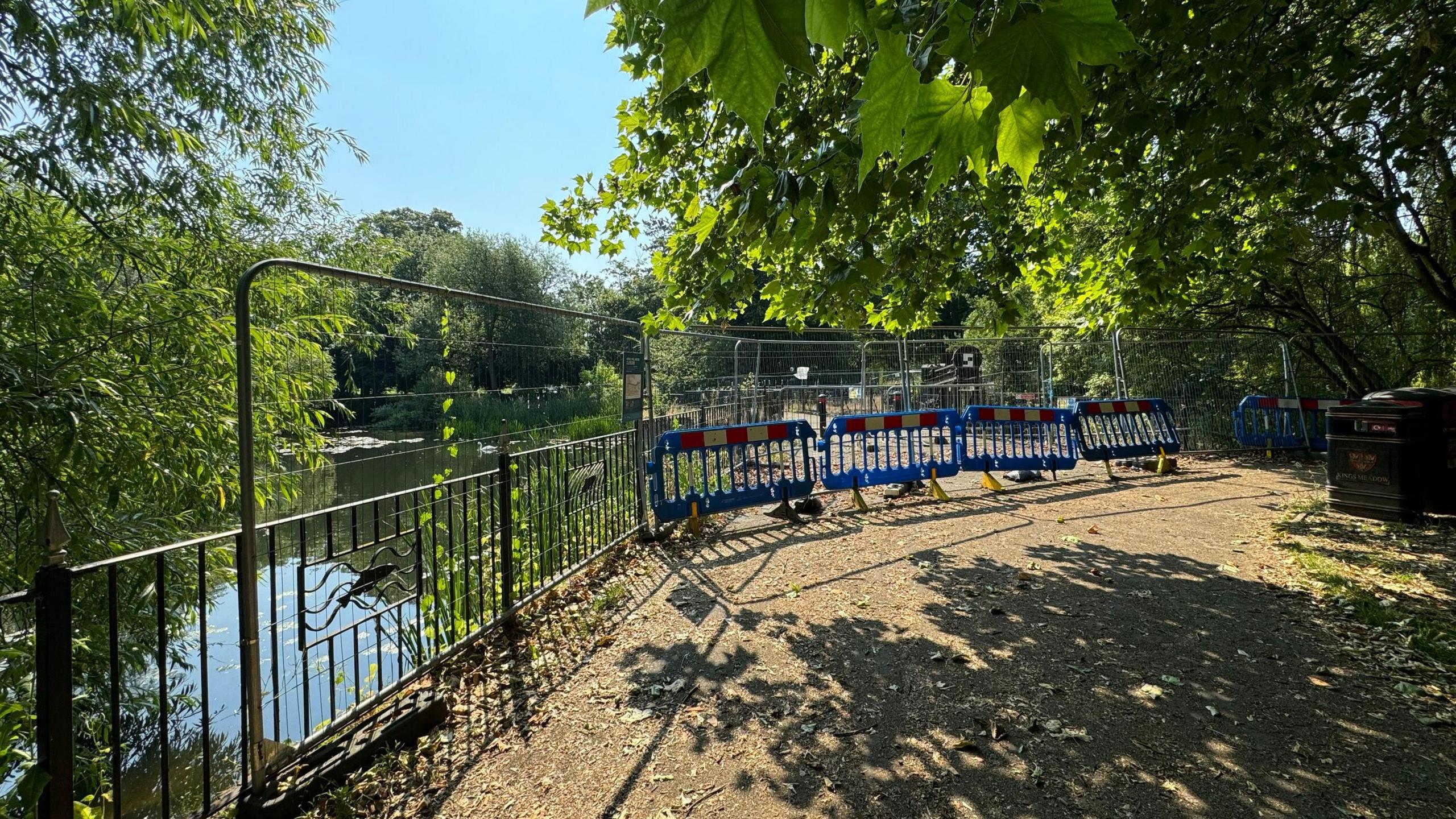 Footbridge closed.  Plastic and metal barriers are closing the footbridge off.  Trees and general foliage surround it.