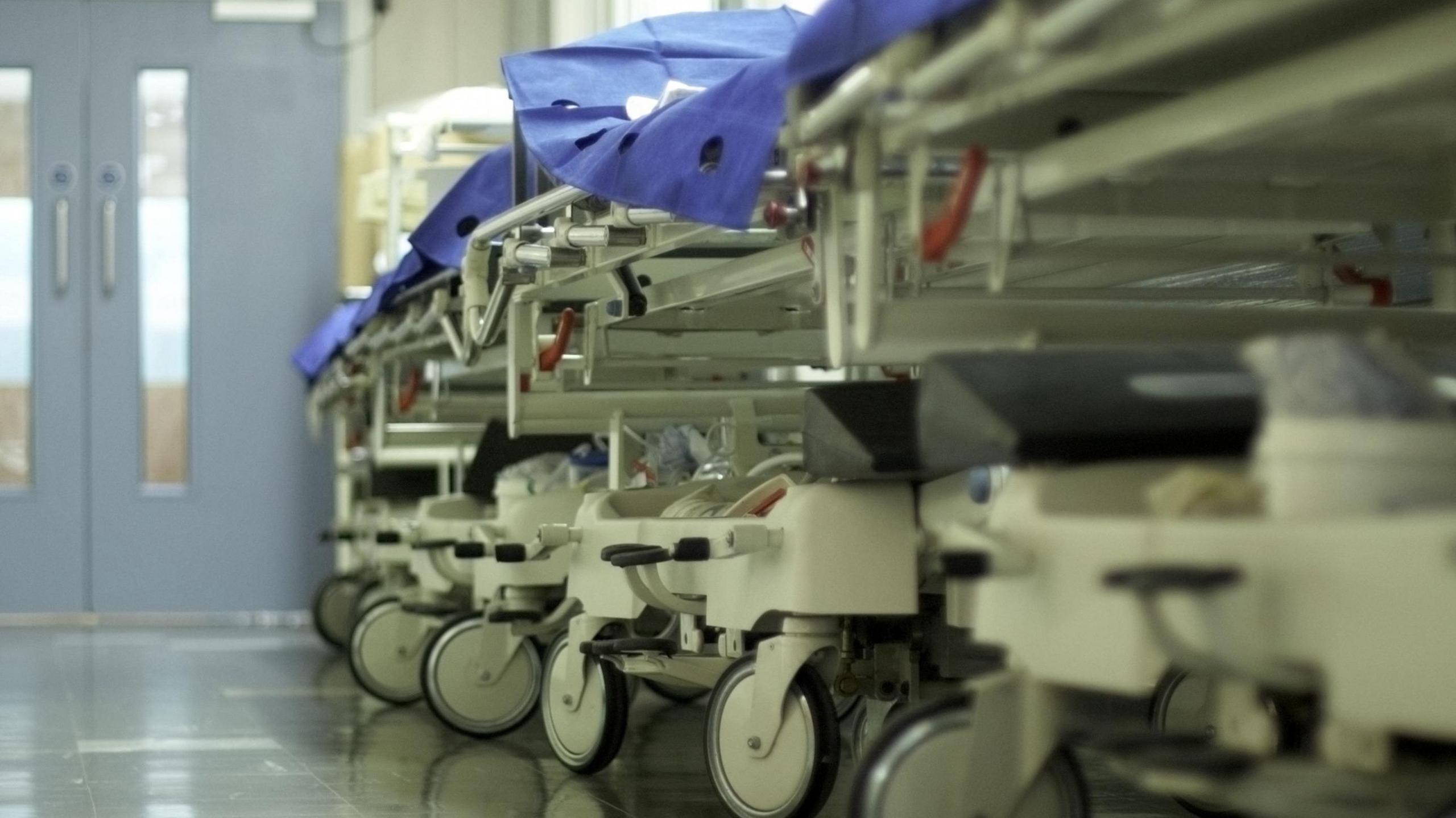 A stock image of a hospital corridor with gurneys and bed trolleys