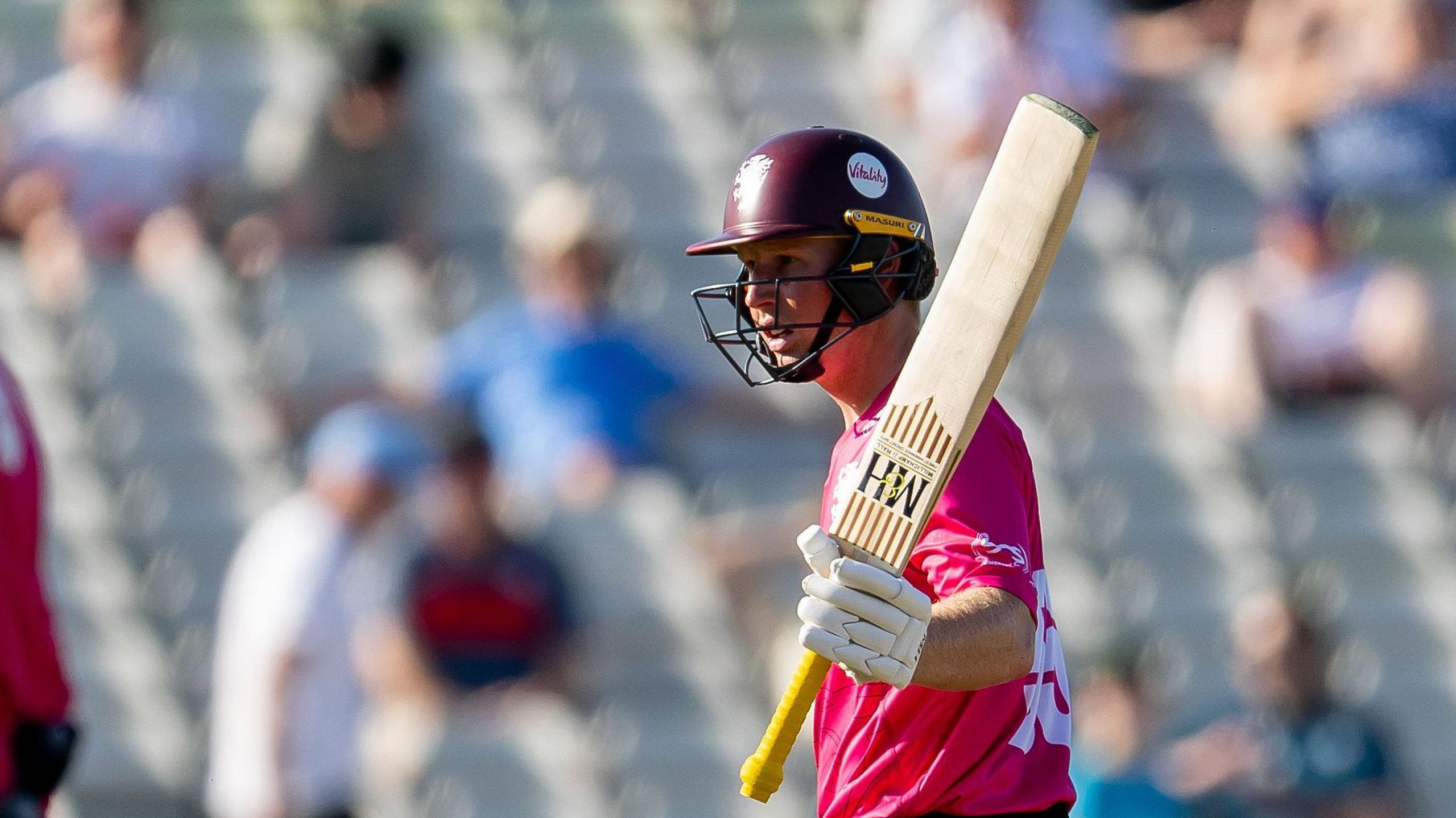 Somerset's James Rew, in a pink shirt, raises his bat after reaching his half century