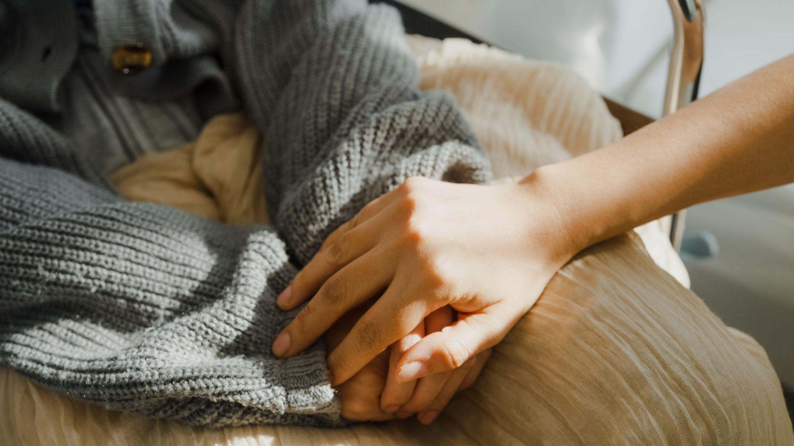 A person placing their hand on top of someone's hands that they have put together on their lap.