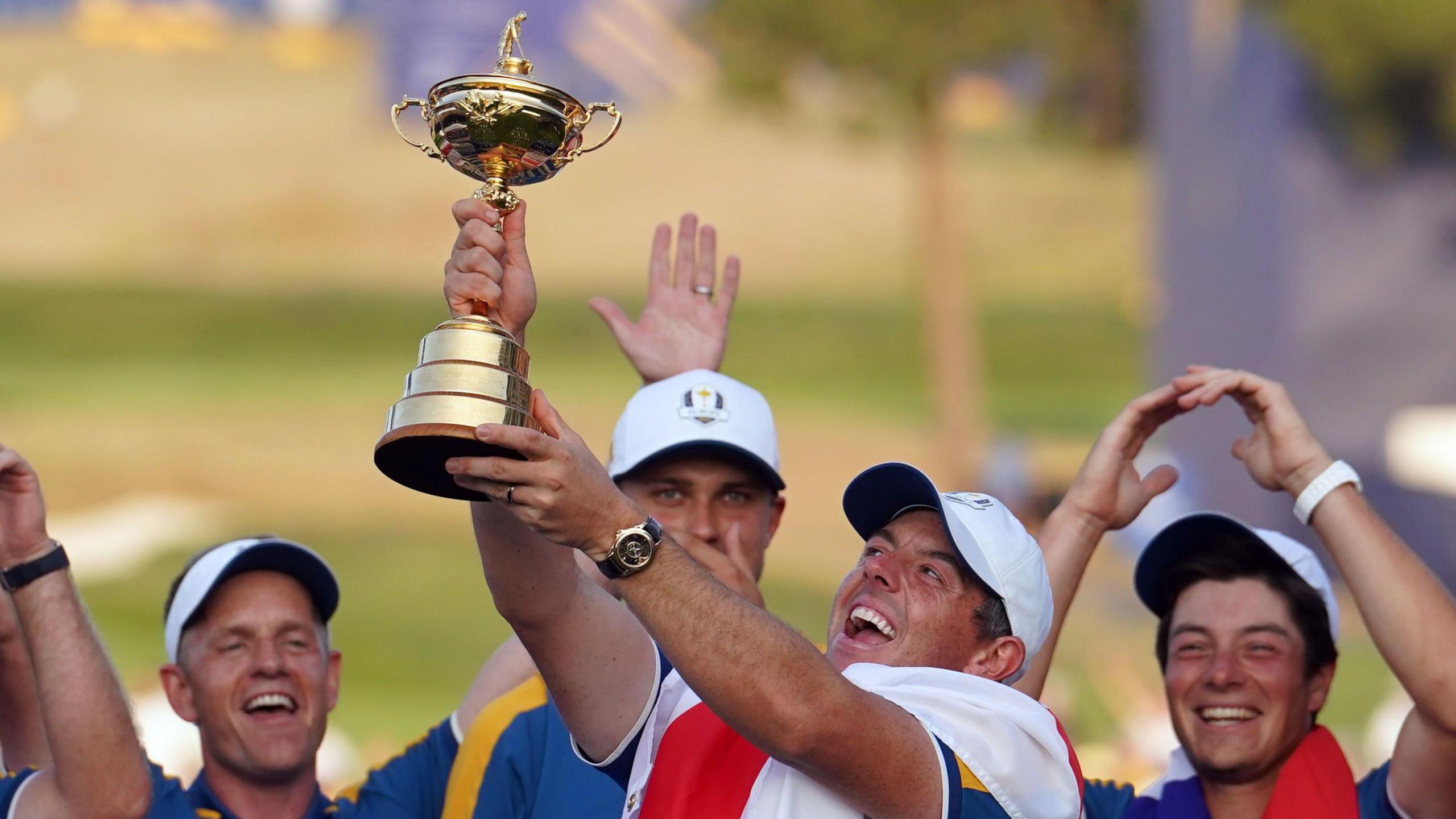 A beaming Rory McIlroy raises the golden Ryder Cup trophy into the air, encouraged by his jubilant European team-mates.