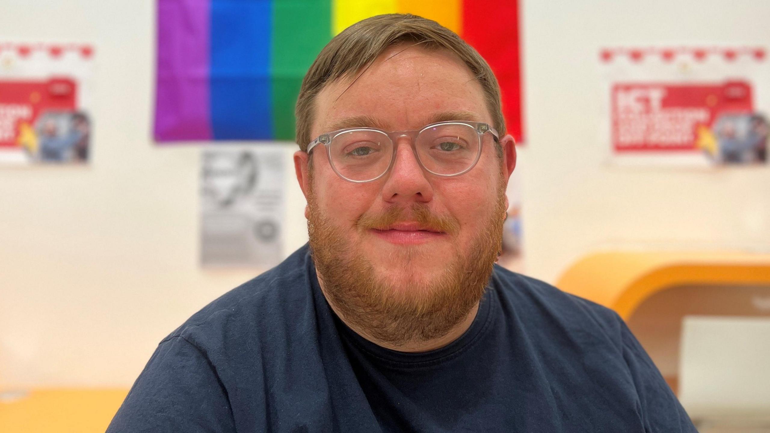 Dean Marsh sitting in front of a rainbow flag