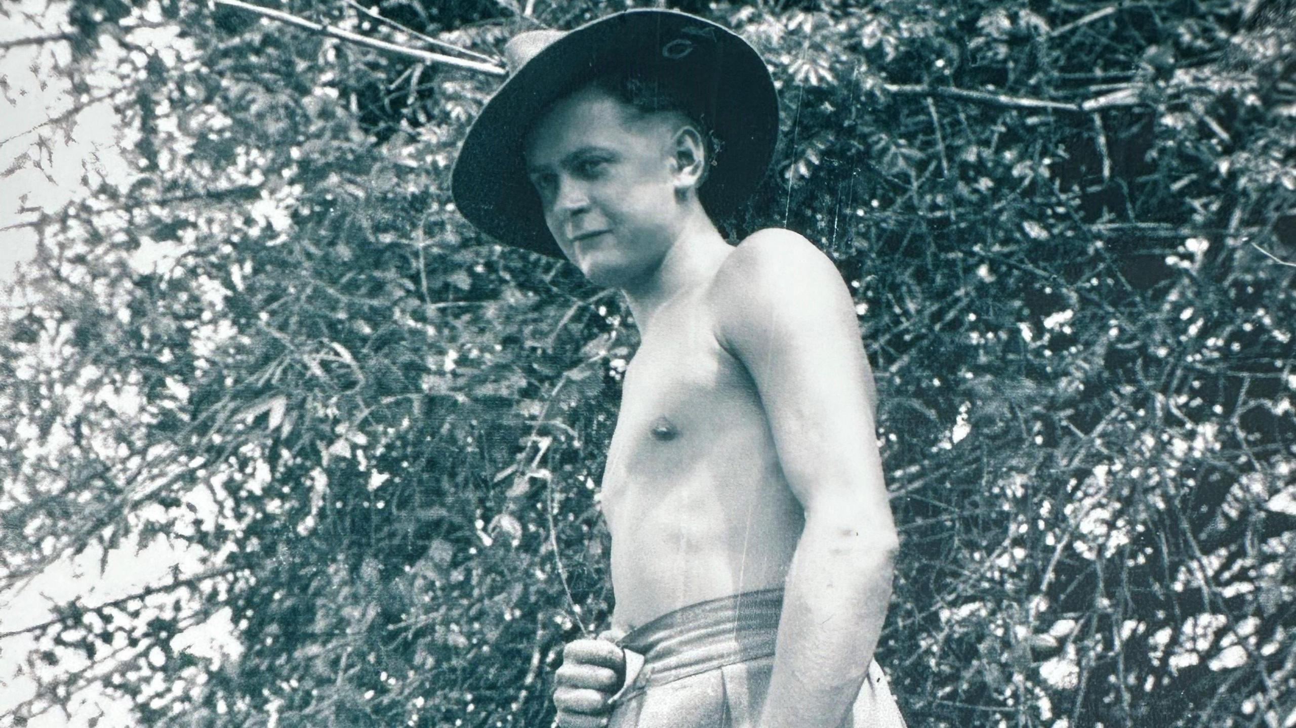 A black and white photograph of a shirtless James Fenton wearing his slouch hat in the jungle in Burma.
