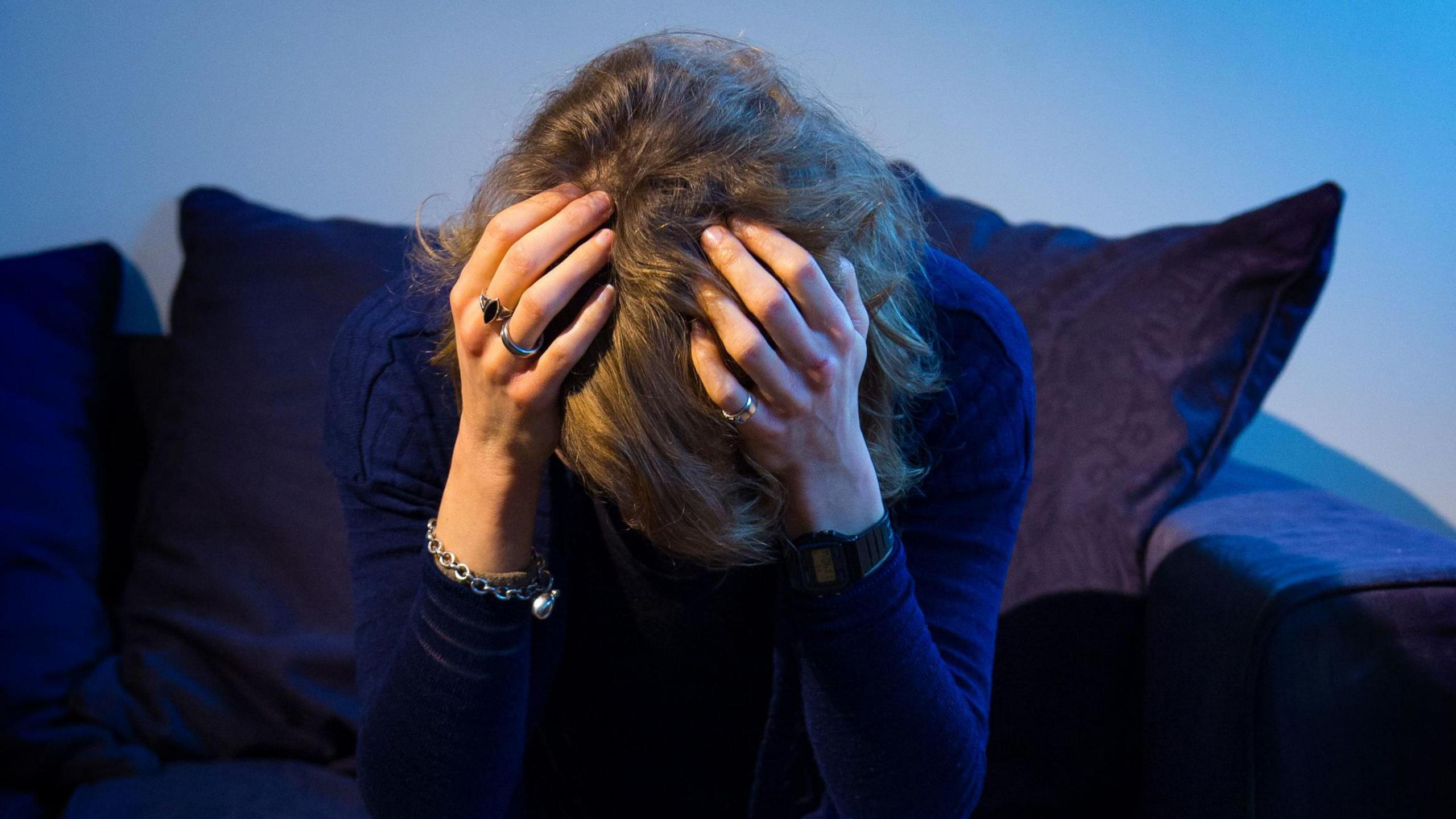 A woman sitting on a navy sofa with her head in her hands.