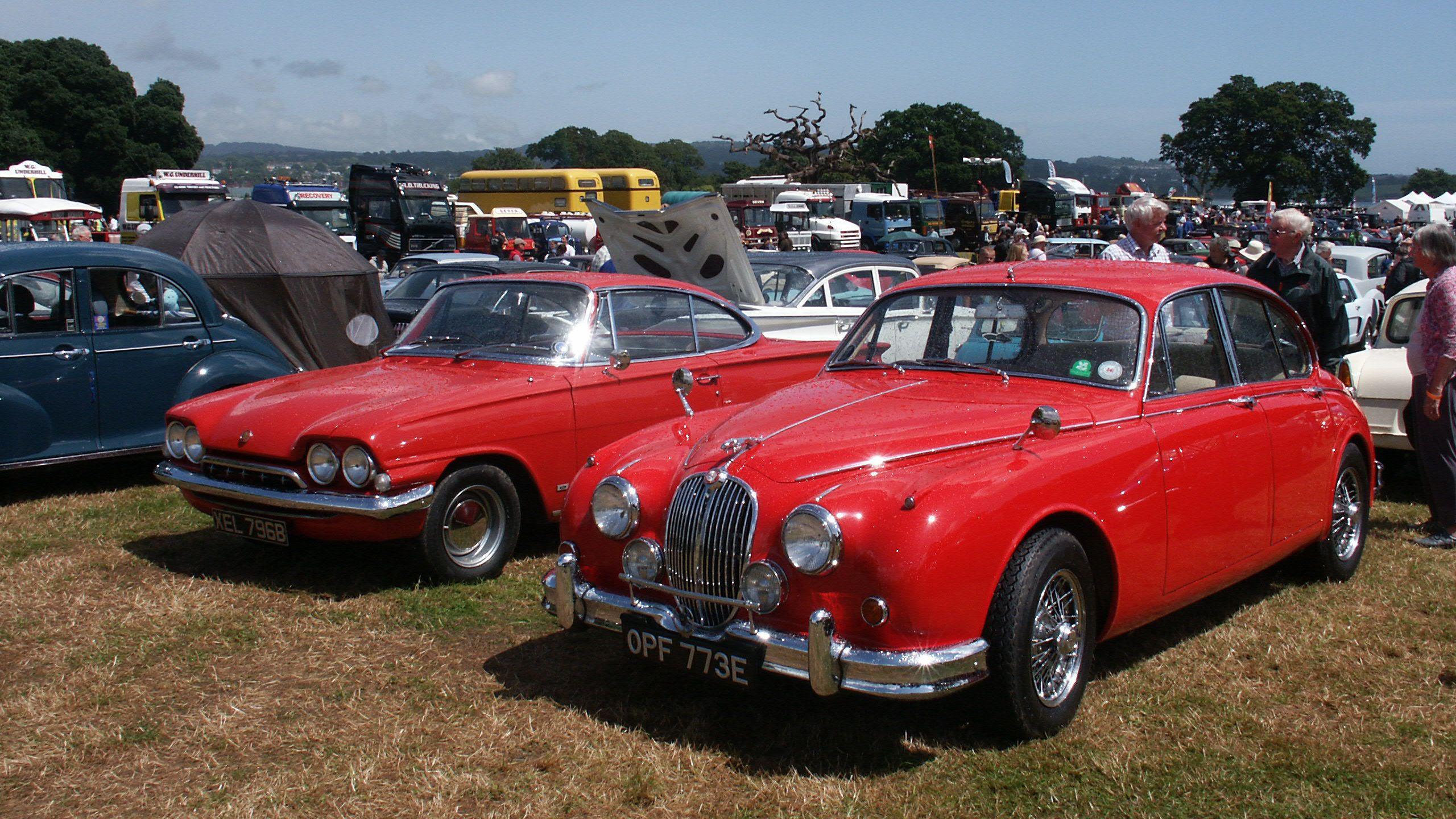 Two red-coloured classic cars in a field at Powderham Castle