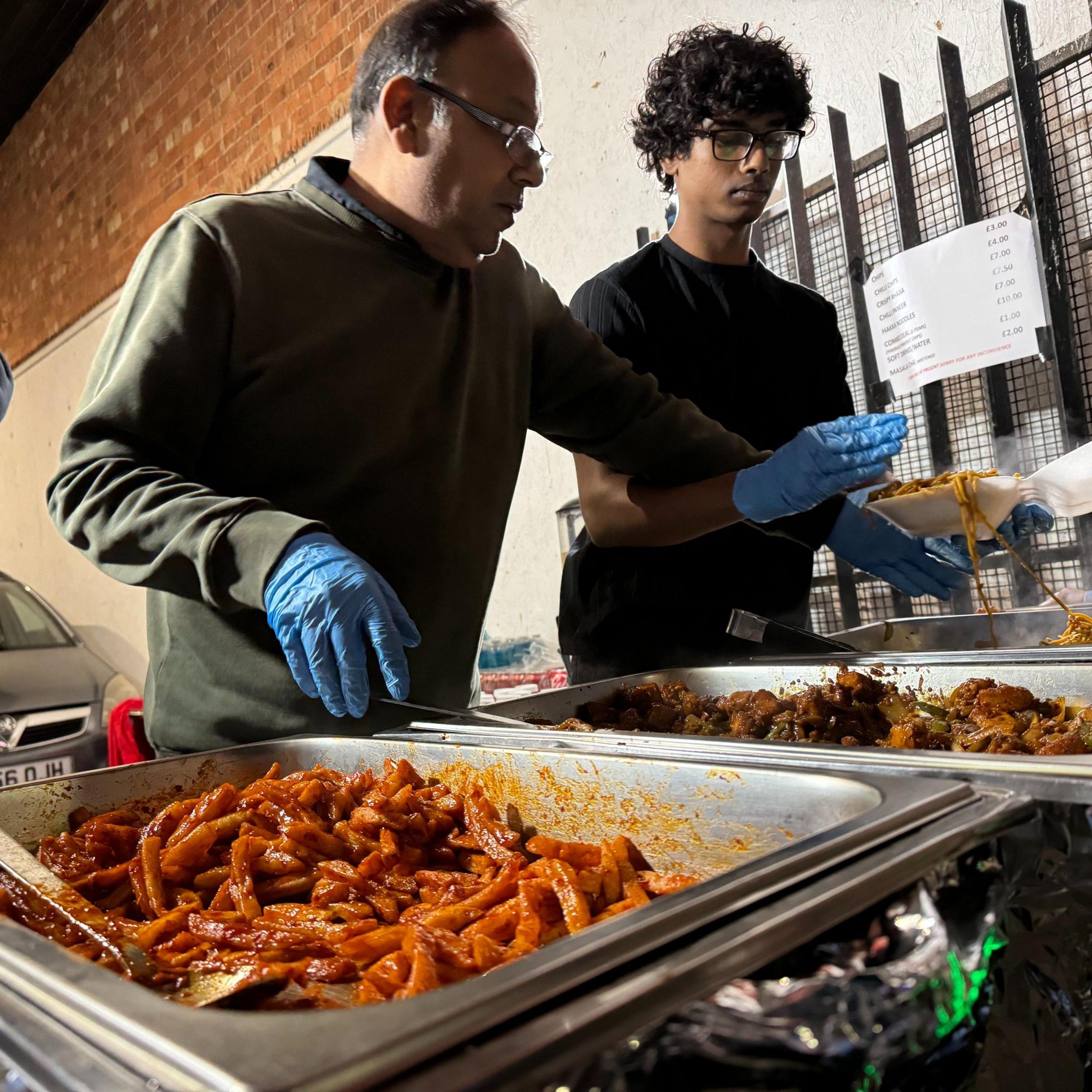 Two men prepare traditional food for people along Belgrave Road